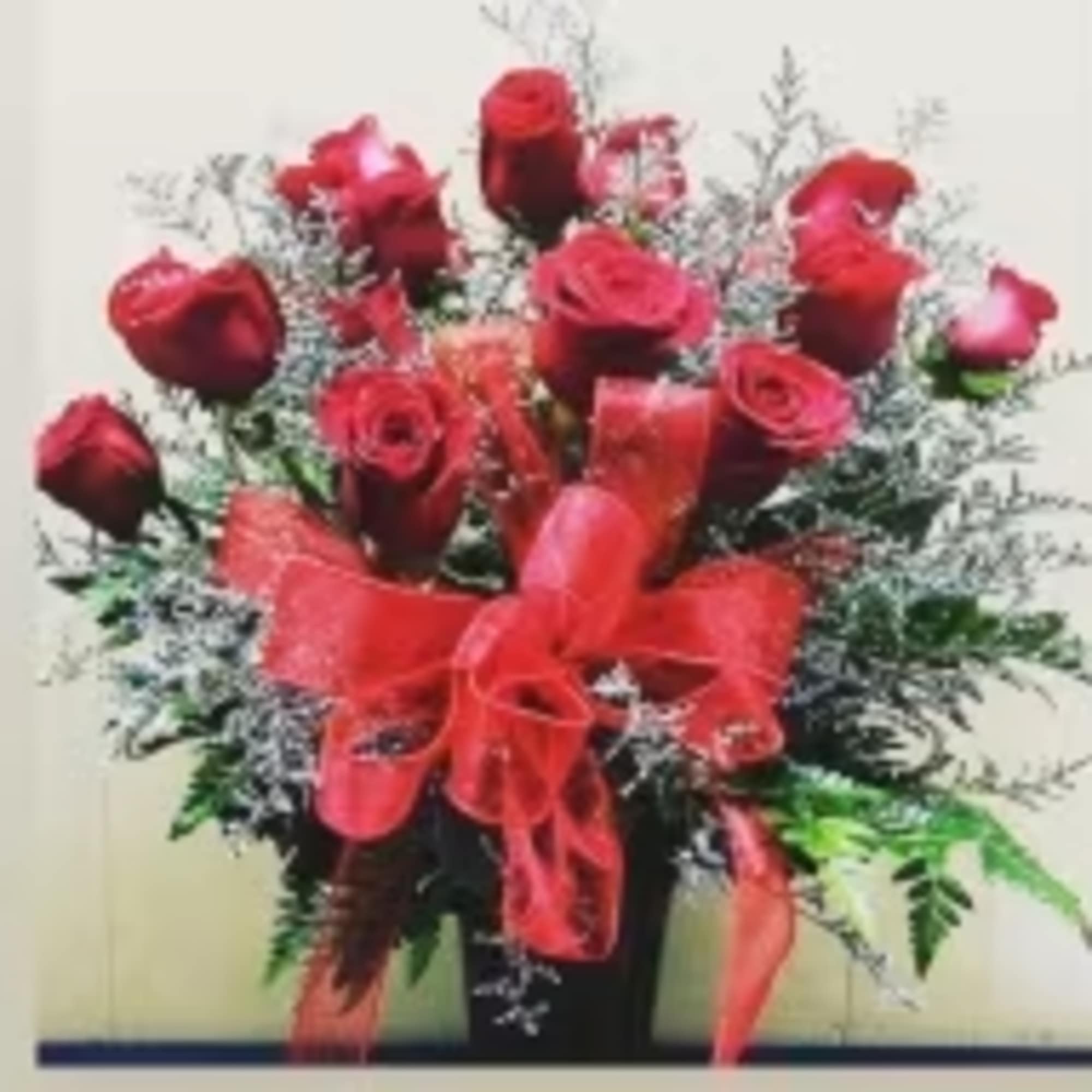 Red roses arranged in a black vase with a red ribbon bow