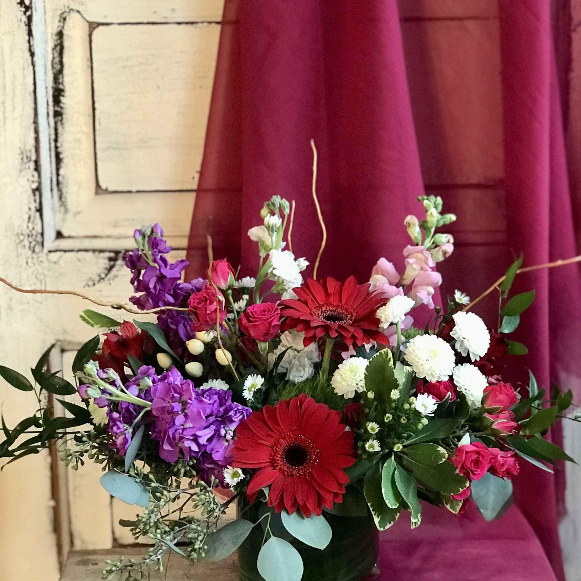 Mixed bouquet with red gerbera daisies, pink roses, and purple flowers in a dark vase
