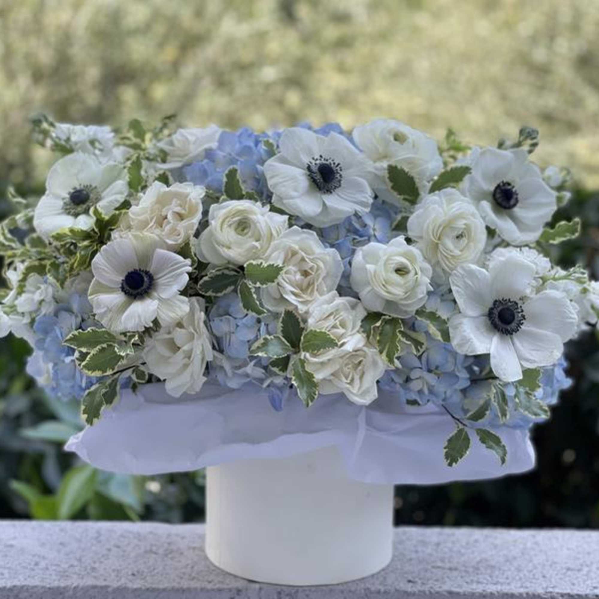 White and pale blue floral arrangement in a white vase
