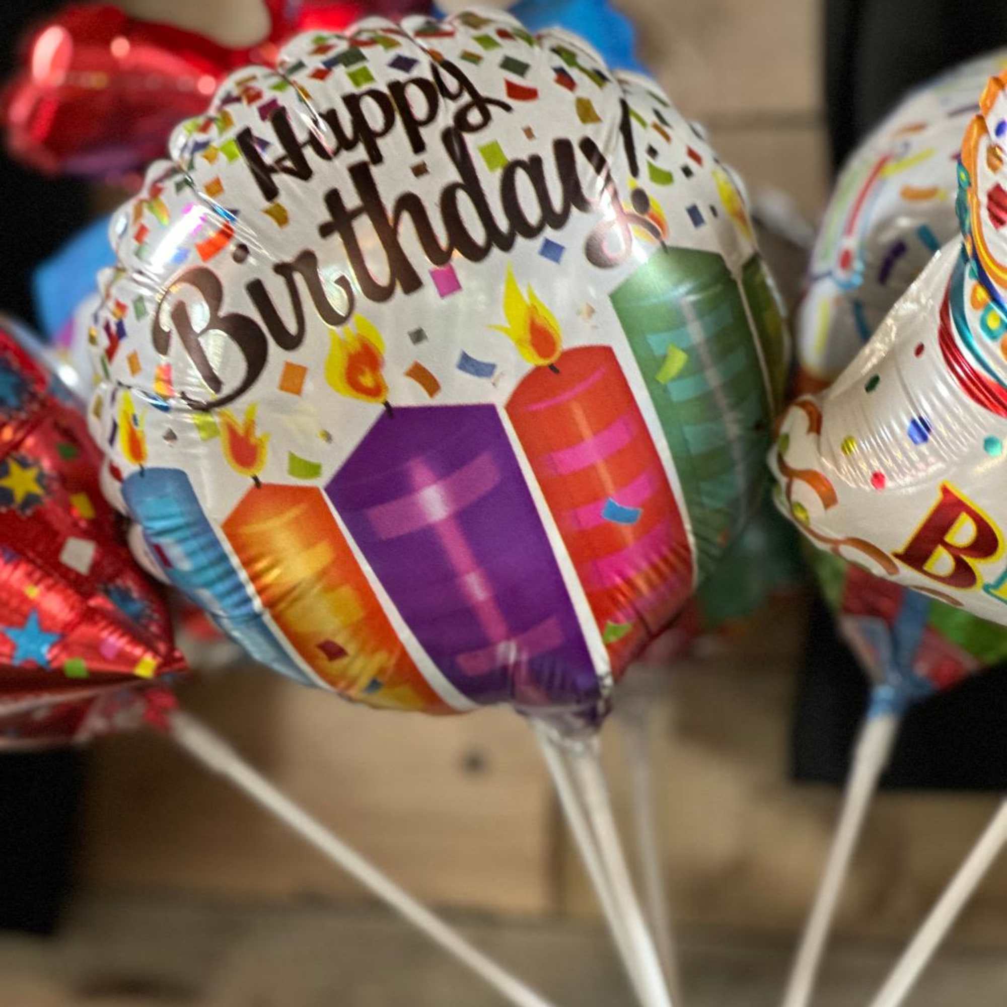 Birthday balloons in a vase, including a "Happy Birthday" balloon with candles