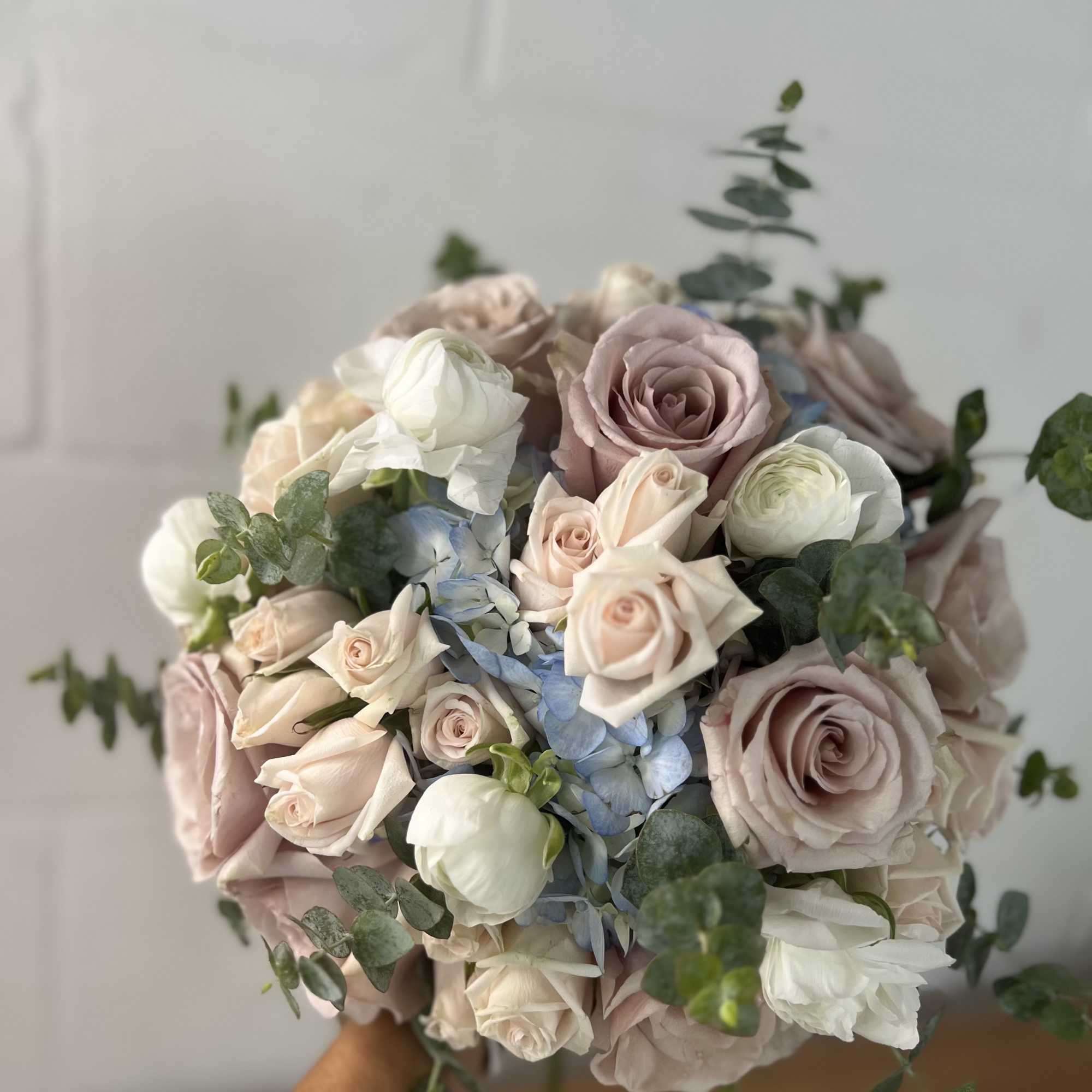 Handheld bouquet of blush and white roses with blue flowers and eucalyptus