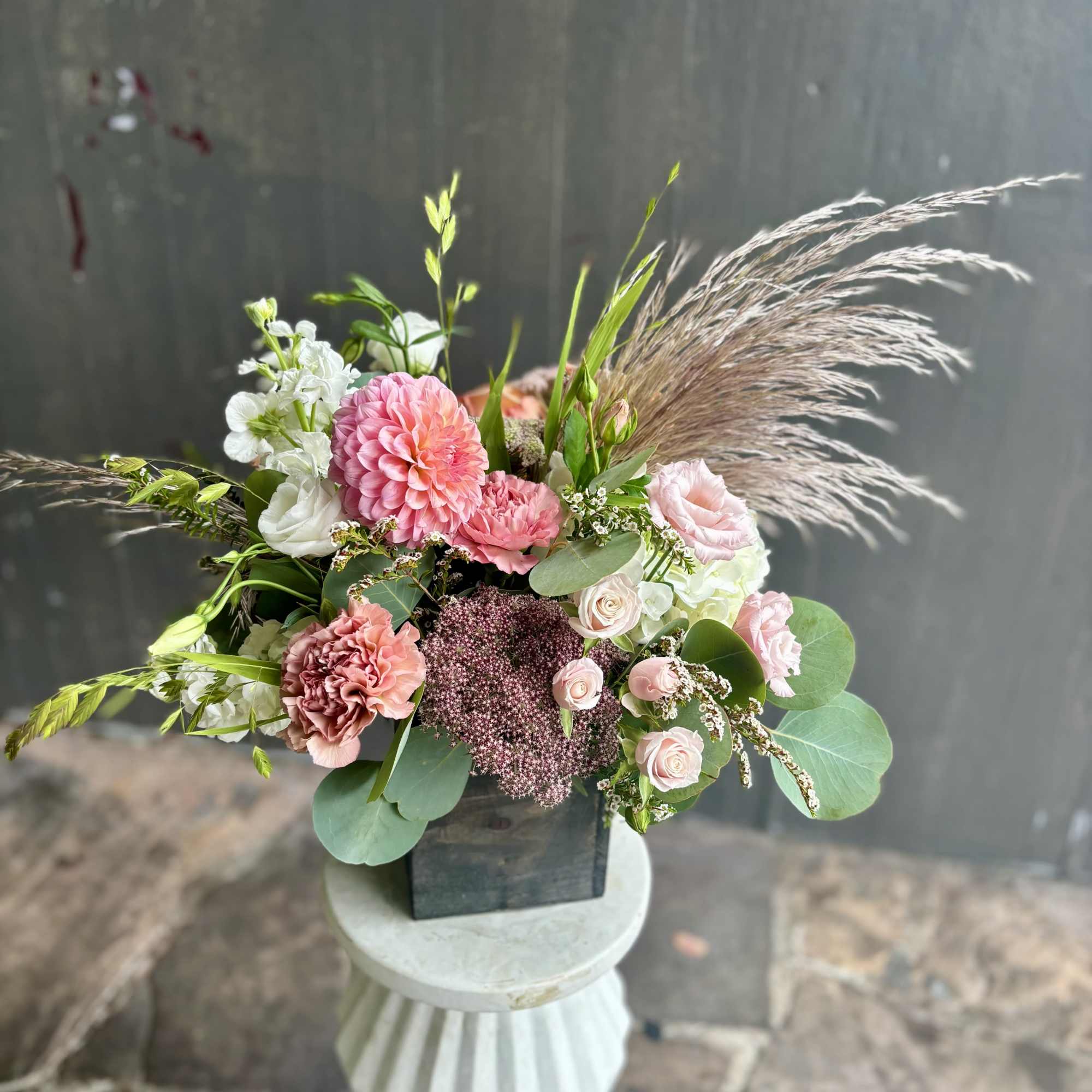 Pink and white floral arrangement in a black container with airy grasses