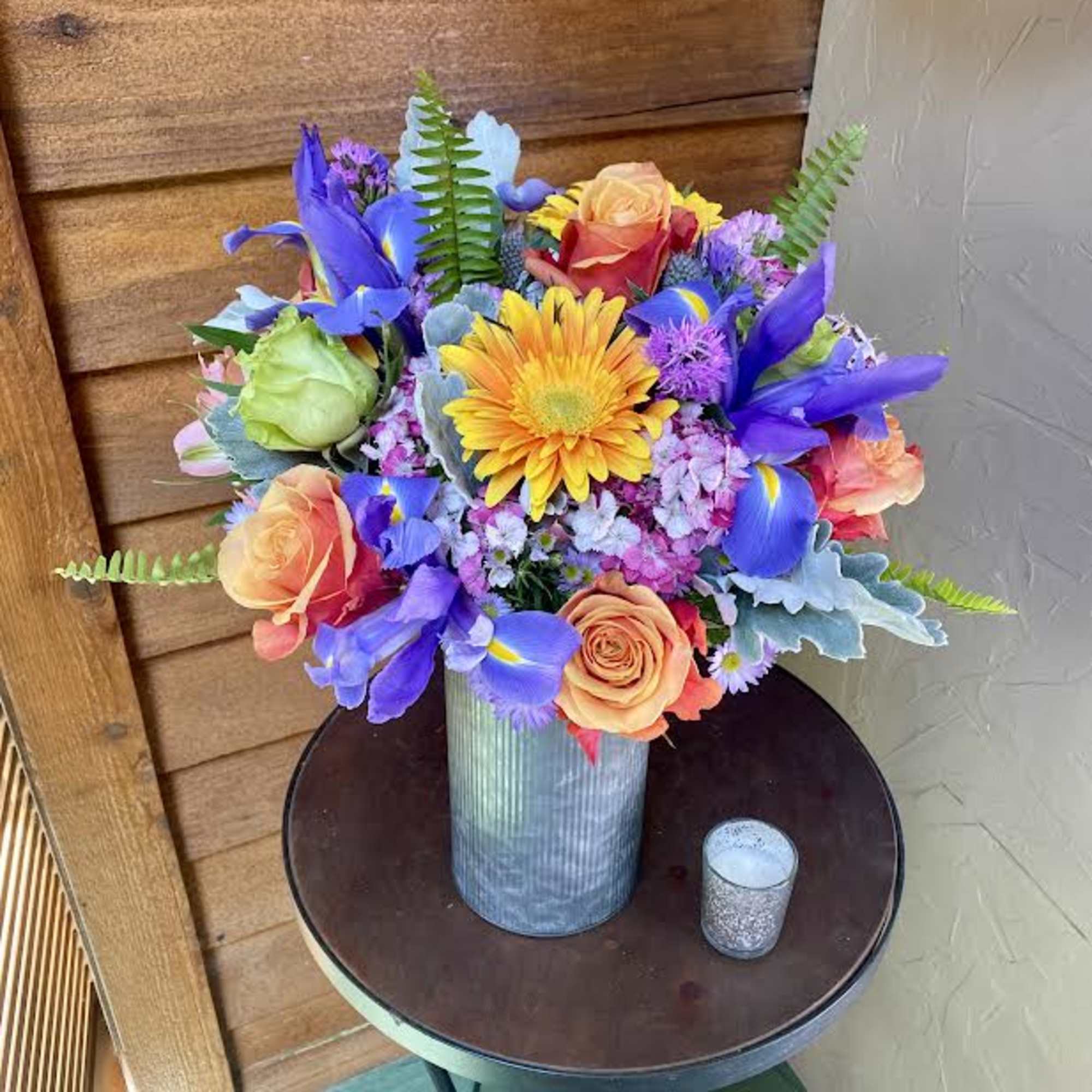 Colorful bouquet in a metal vase with roses, iris, and a yellow daisy.