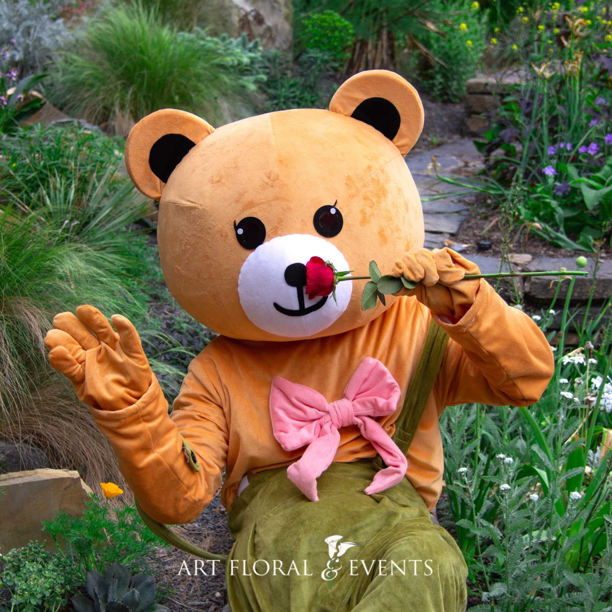 Person in a teddy bear costume holding a red rose in a garden