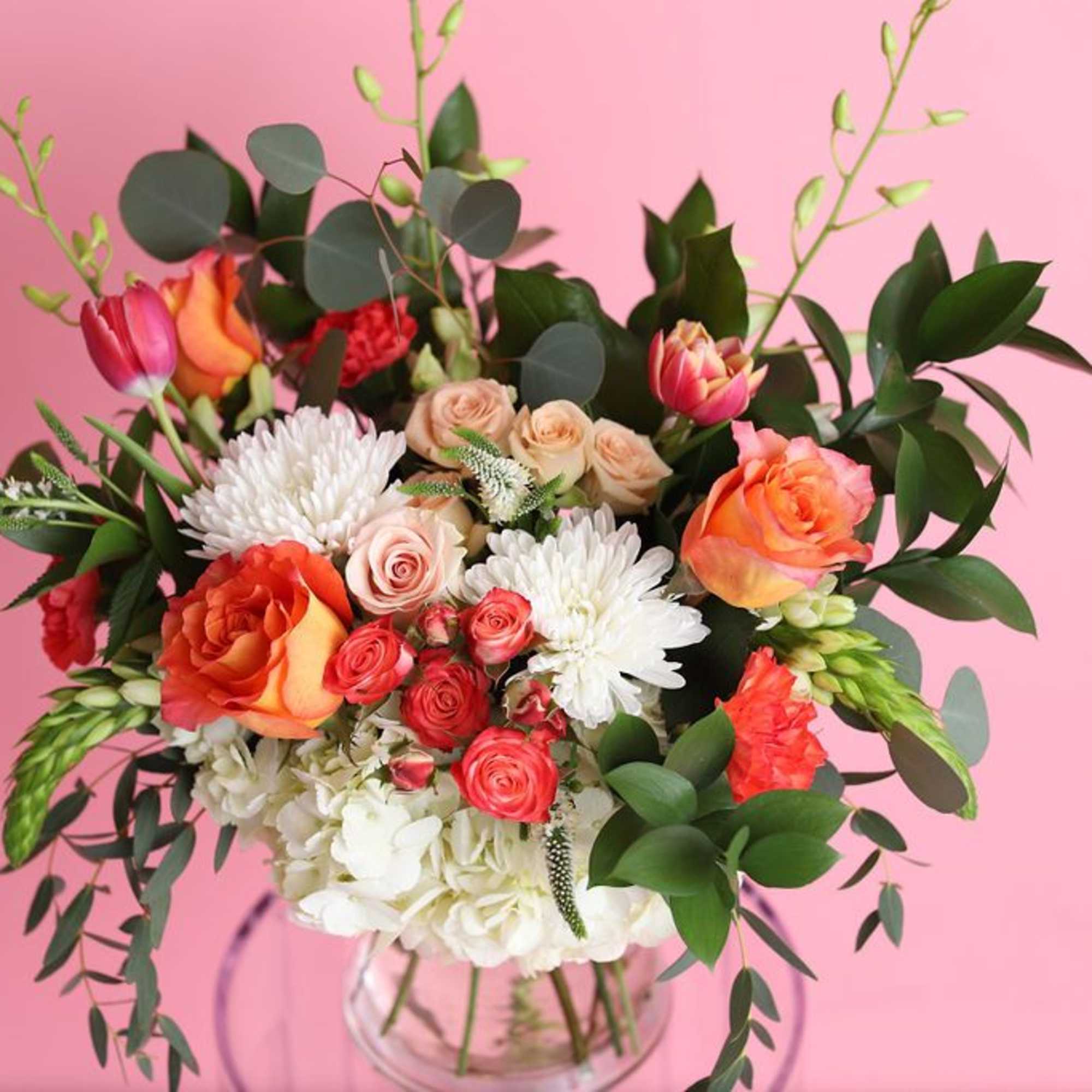Bouquet of orange and pink roses with white blooms in a clear vase