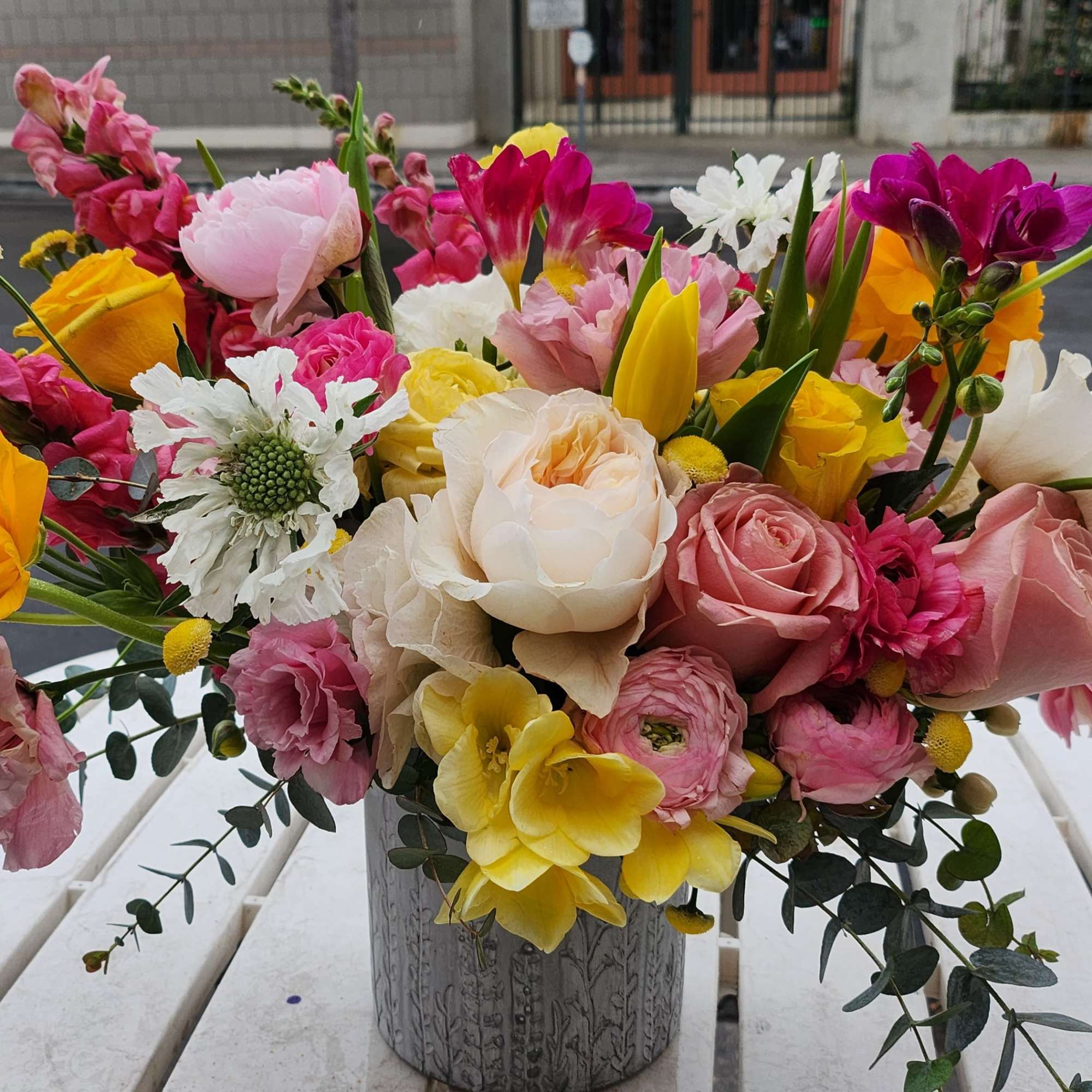 Colorful mixed bouquet of pink, yellow, and white flowers in a gray patterned vase on a table