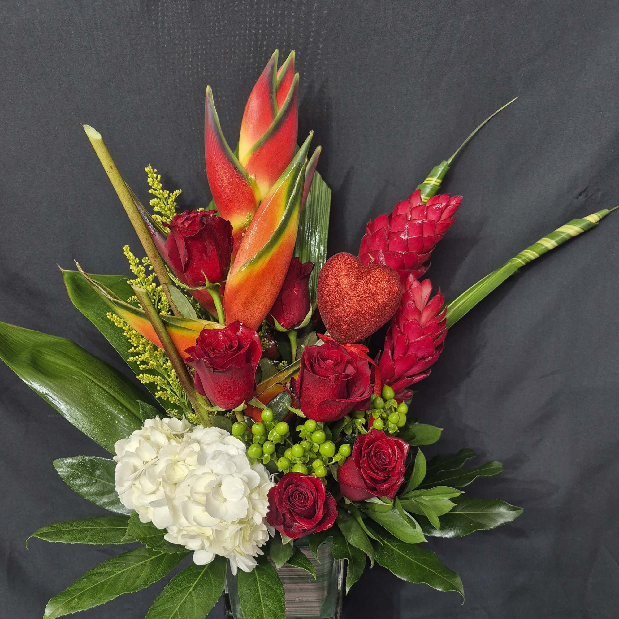Red roses and white hydrangea in a glass vase with tropical blooms and a glitter heart