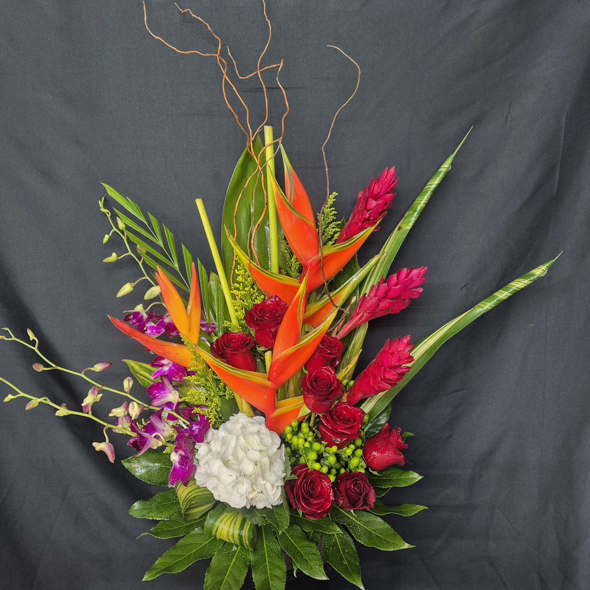 Tropical bouquet with orange heliconia, red roses, purple orchids, and white hydrangea