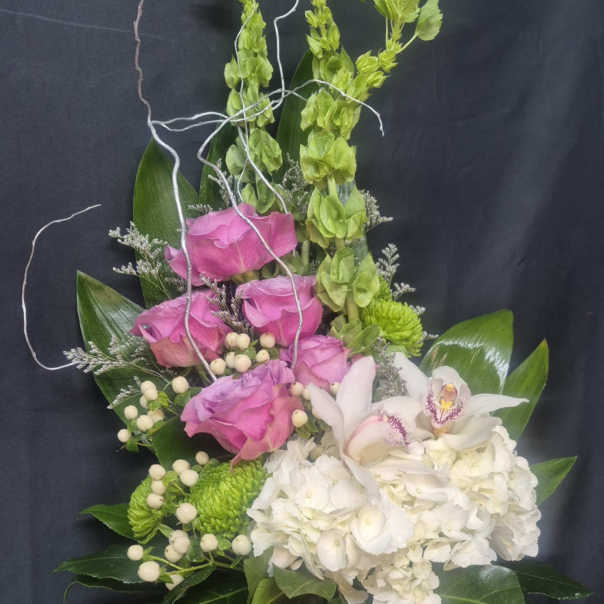 Pink roses, white orchids, and hydrangea in a glass vase with green accents