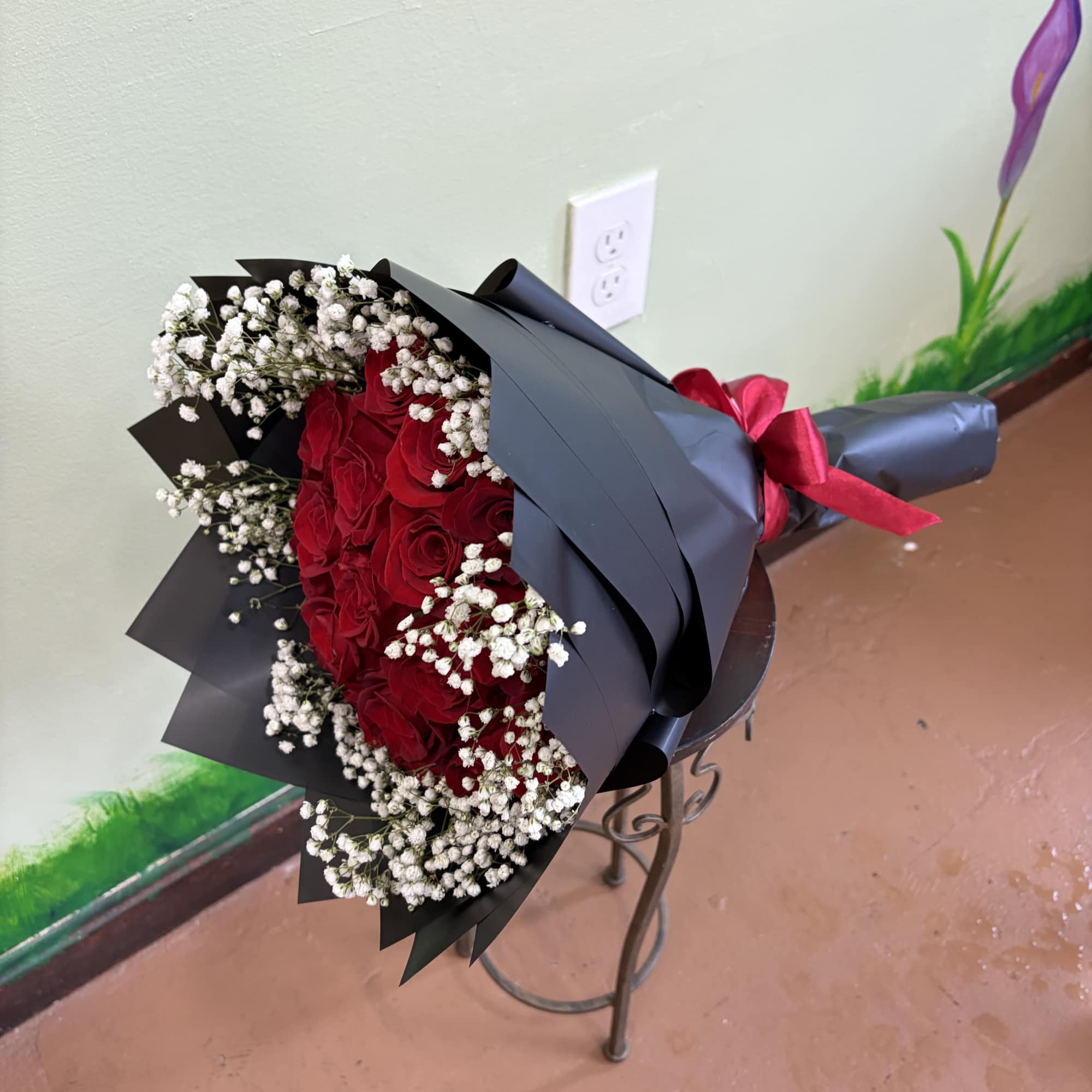 Hand-tied bouquet of red roses with white filler flowers wrapped in black paper and tied with a red ribbon