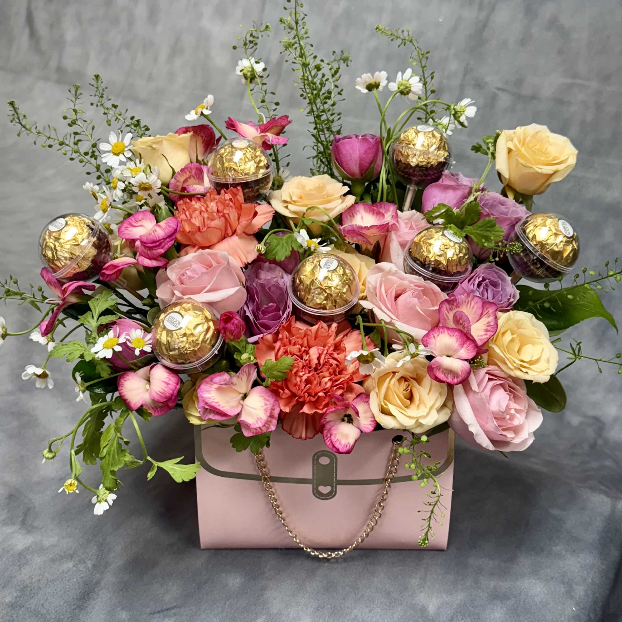 Mixed roses and carnations in a pink gift box with gold-wrapped chocolates