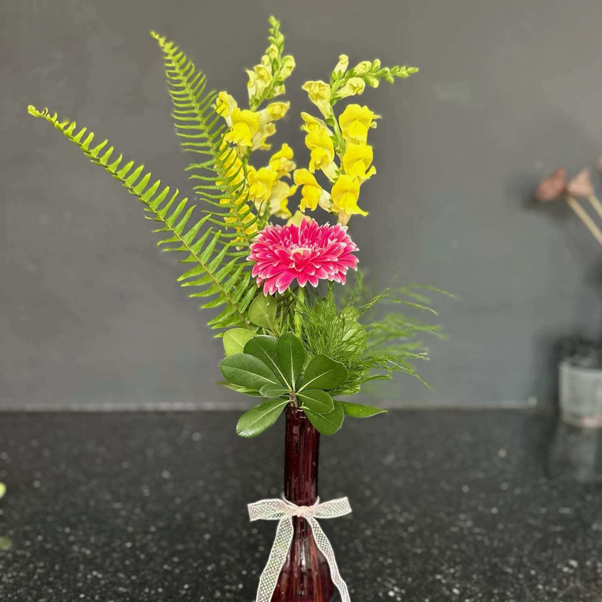 Pink gerbera daisy and yellow snapdragons in a red vase