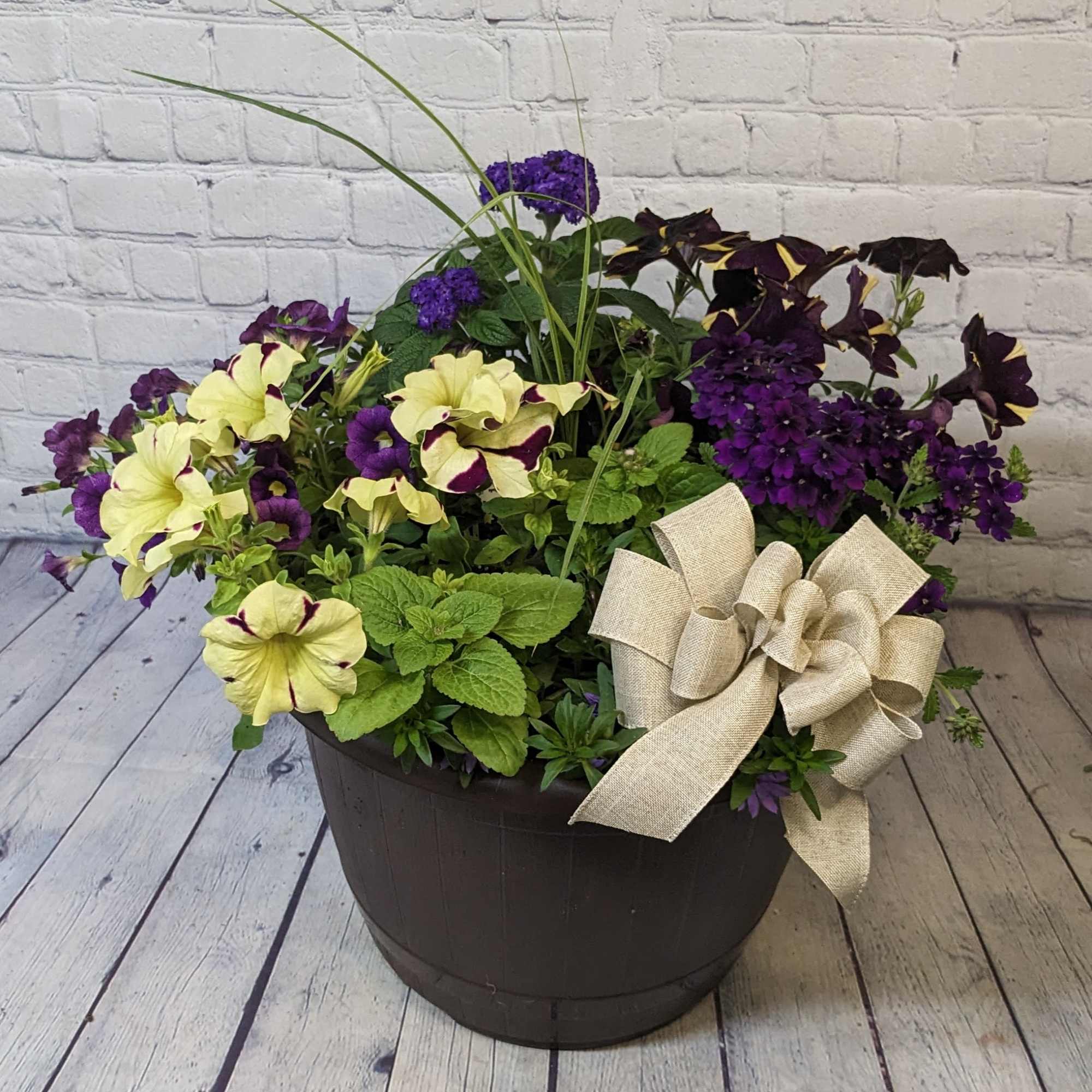 Purple and pale yellow petunias in a dark planter with a burlap bow