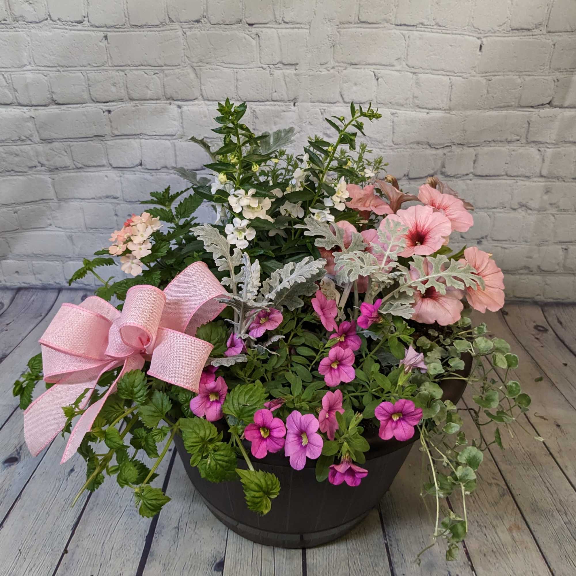 Mixed pink and white flowers in a black planter with a pink bow