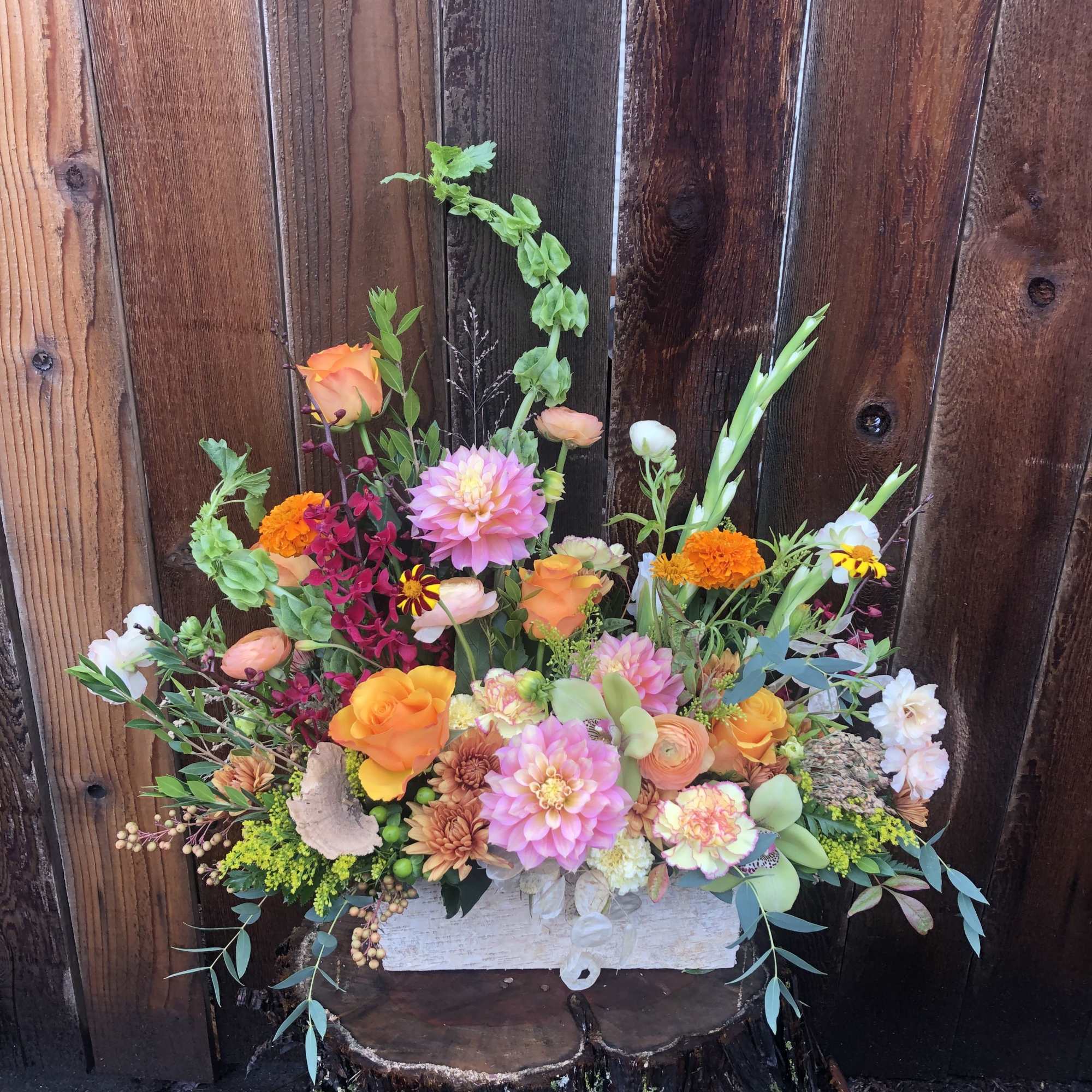 Rustic rectangular arrangement of orange roses, pink dahlias and mixed flowers in a white box on a wood stump