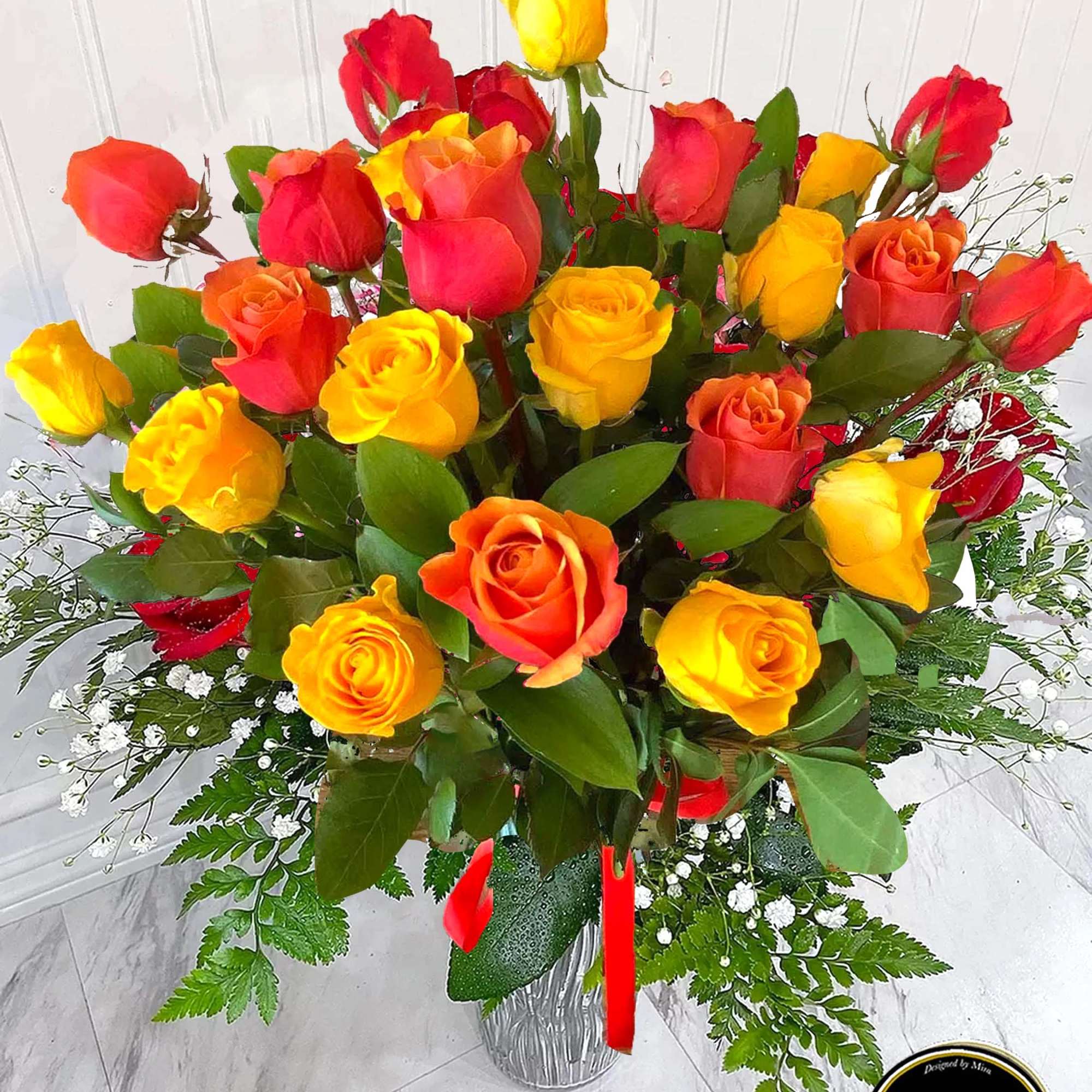 Tall arrangement of red, orange, and yellow roses in a clear glass vase