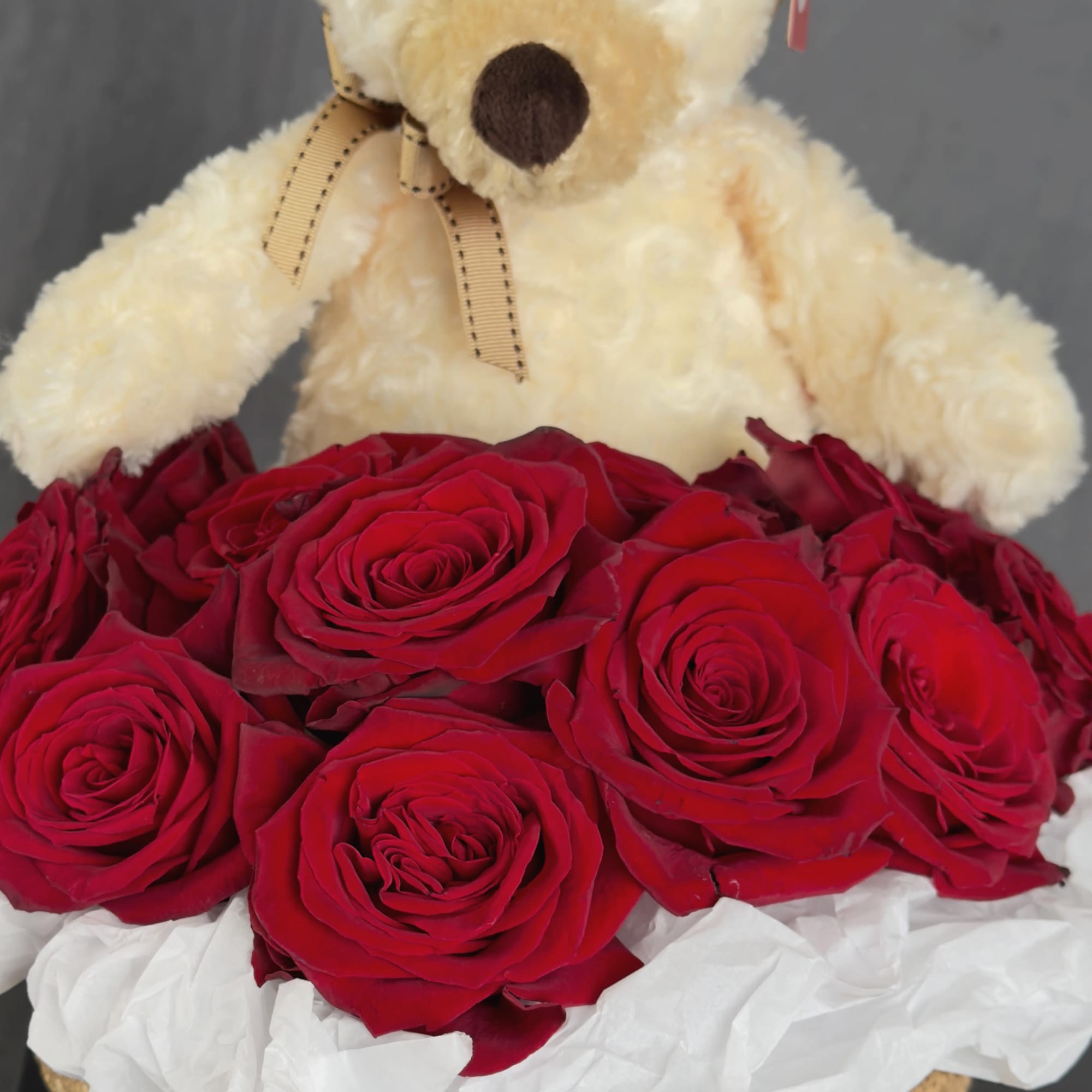 Teddy bear above a basket of red roses