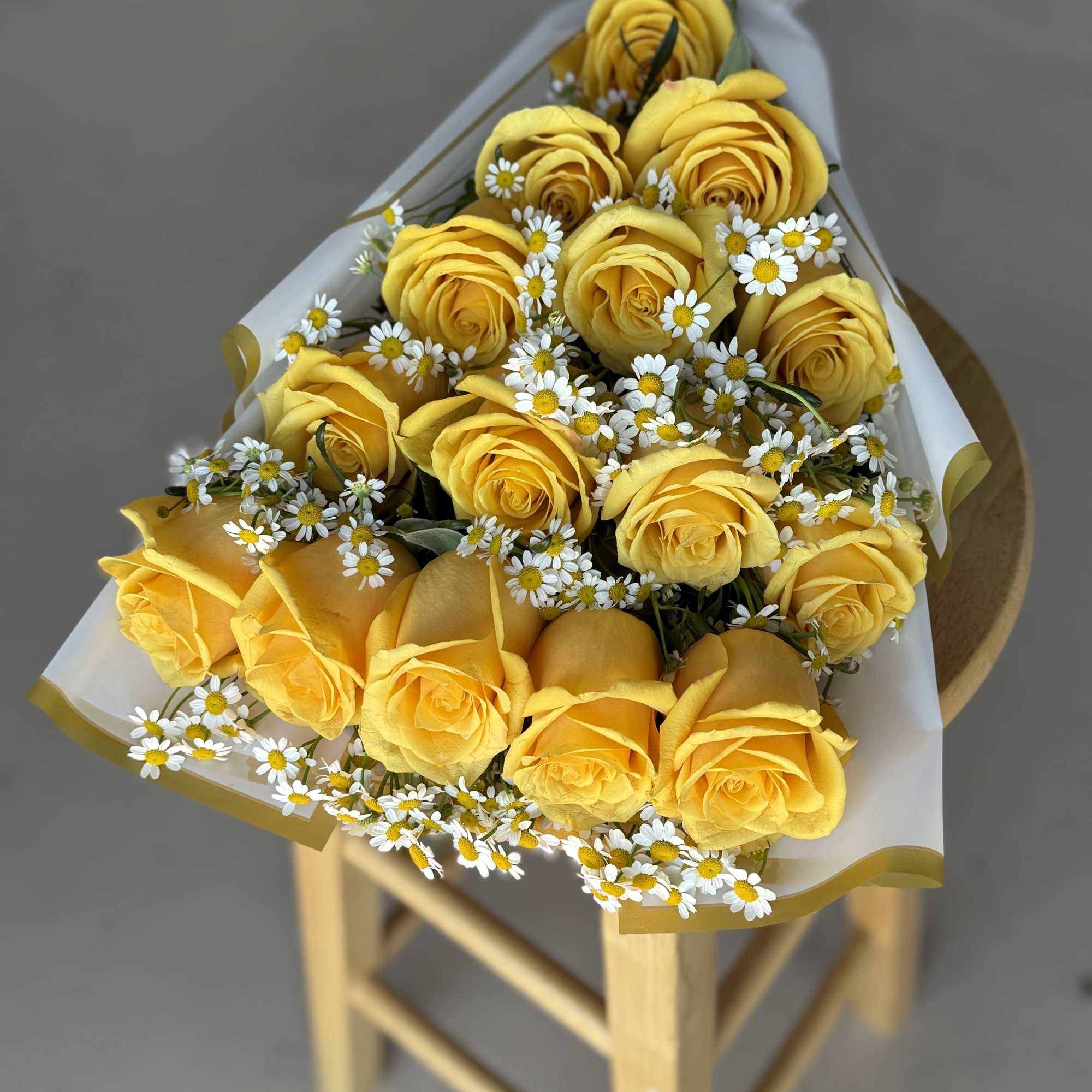 Bouquet of yellow roses with small white daisies wrapped in white paper