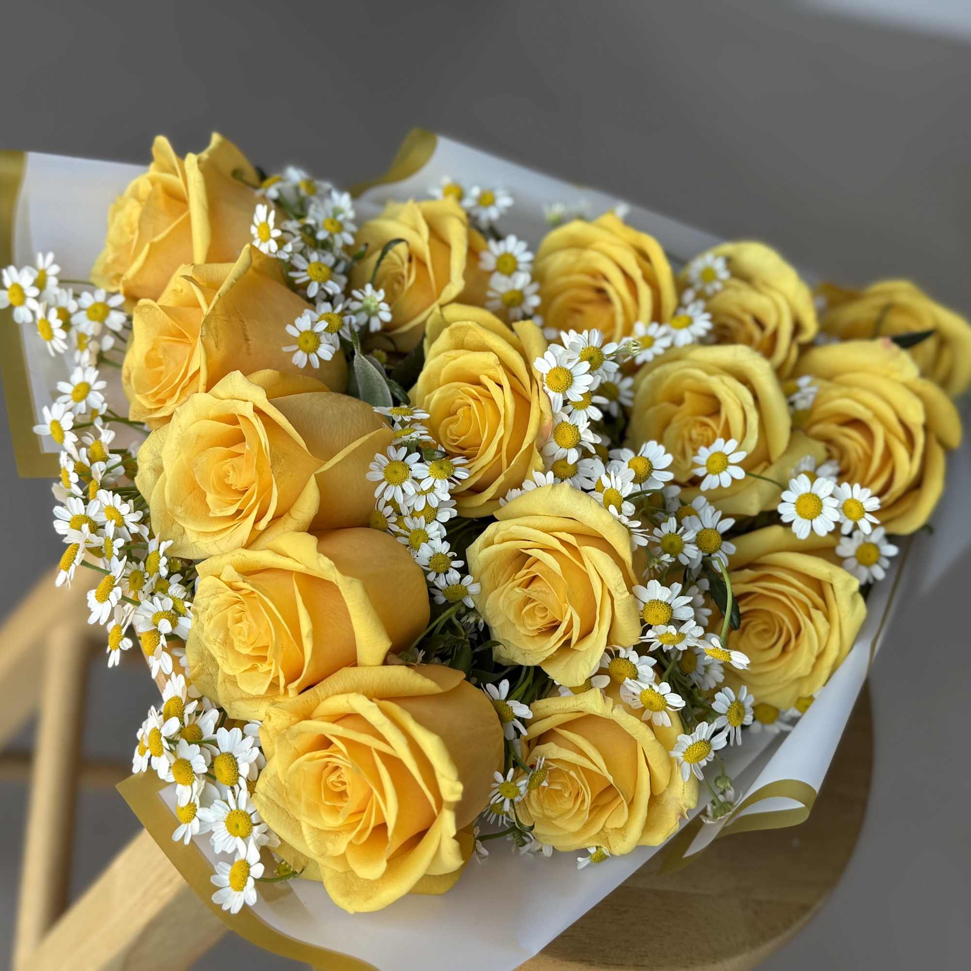 Bouquet of yellow roses and small white daisies wrapped in white paper