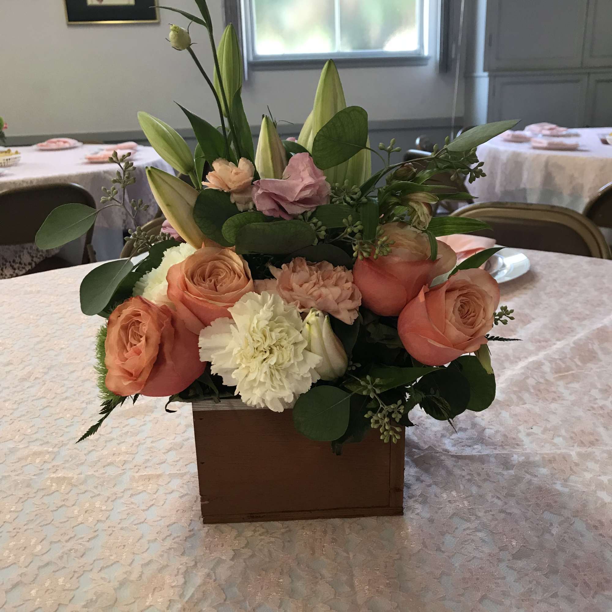 A low, romantic centerpiece in a rectangular wooden box blends peach roses