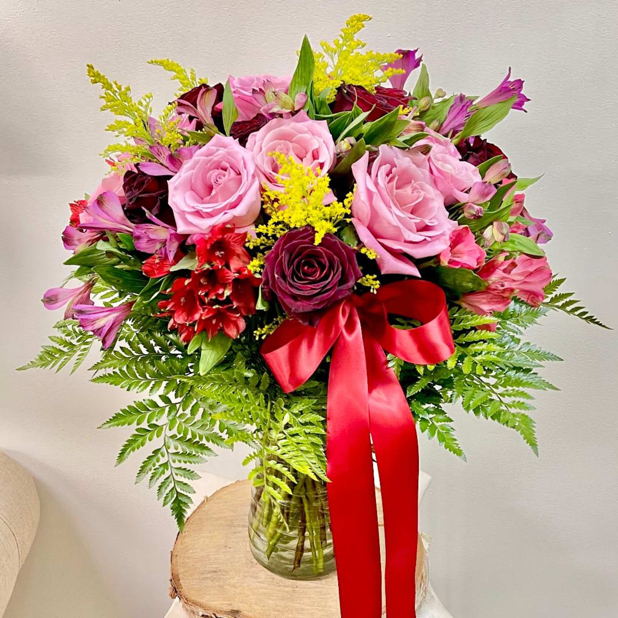 Pink and burgundy rose bouquet in a glass vase with a red ribbon