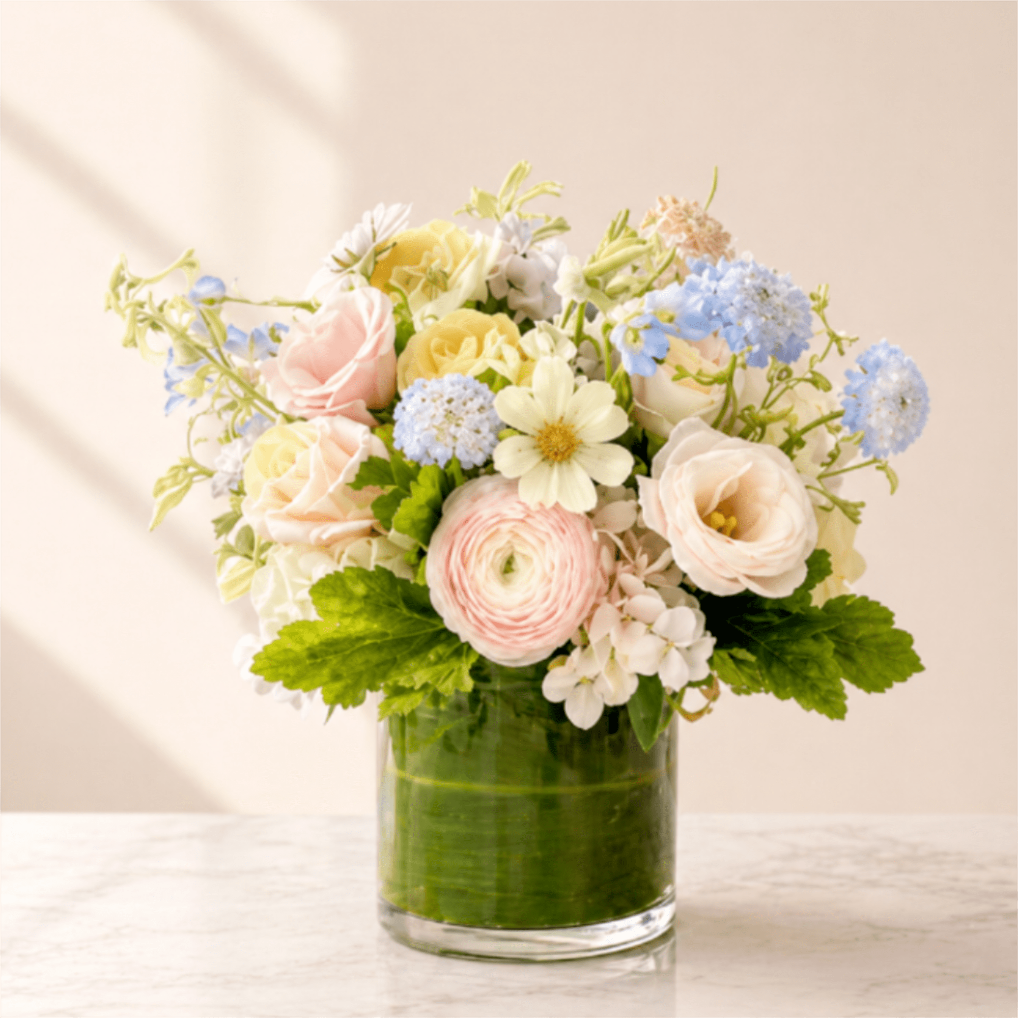 Pastel bouquet of roses, ranunculus, and blue blooms in a glass vase