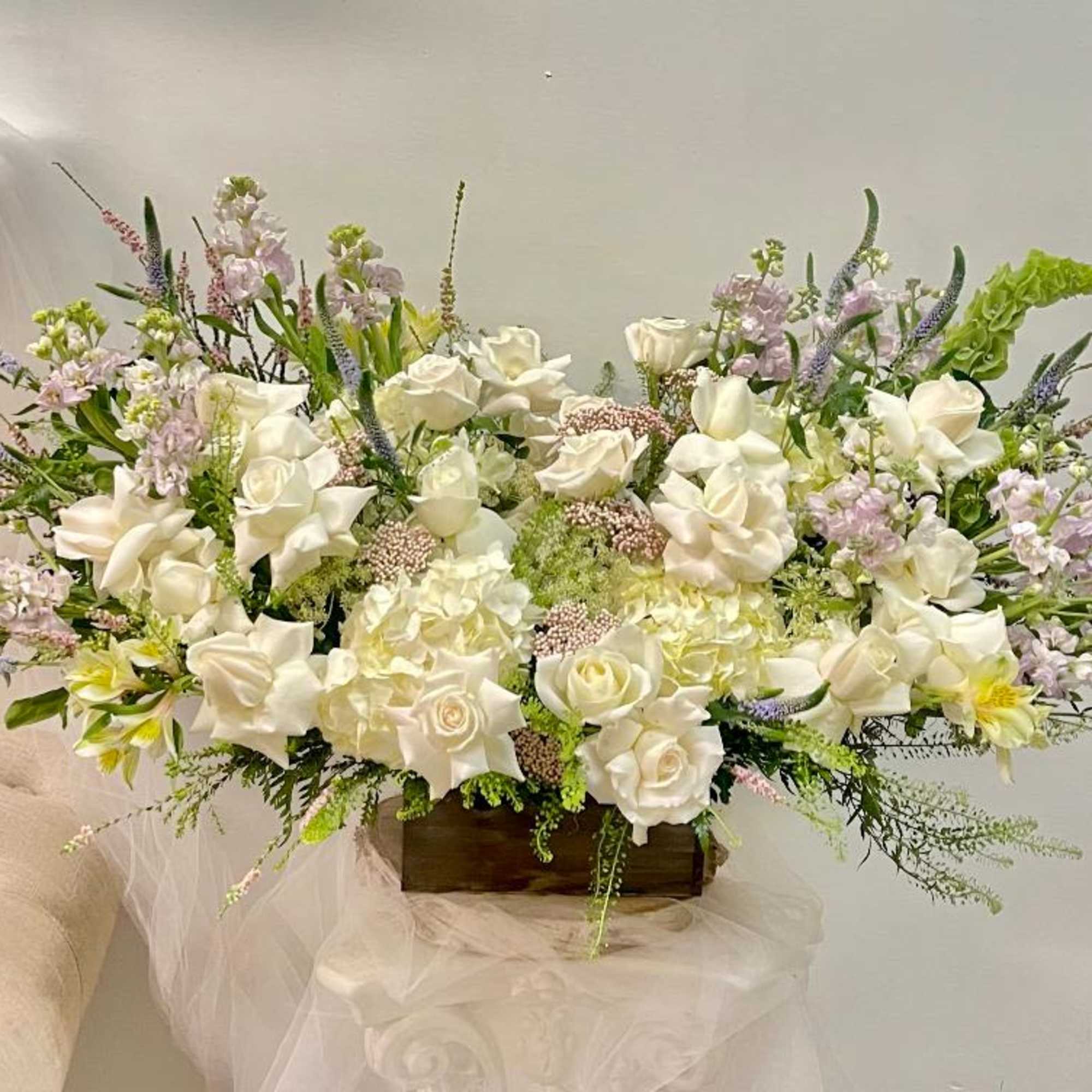 Large white floral arrangement in a wooden container with pastel accents