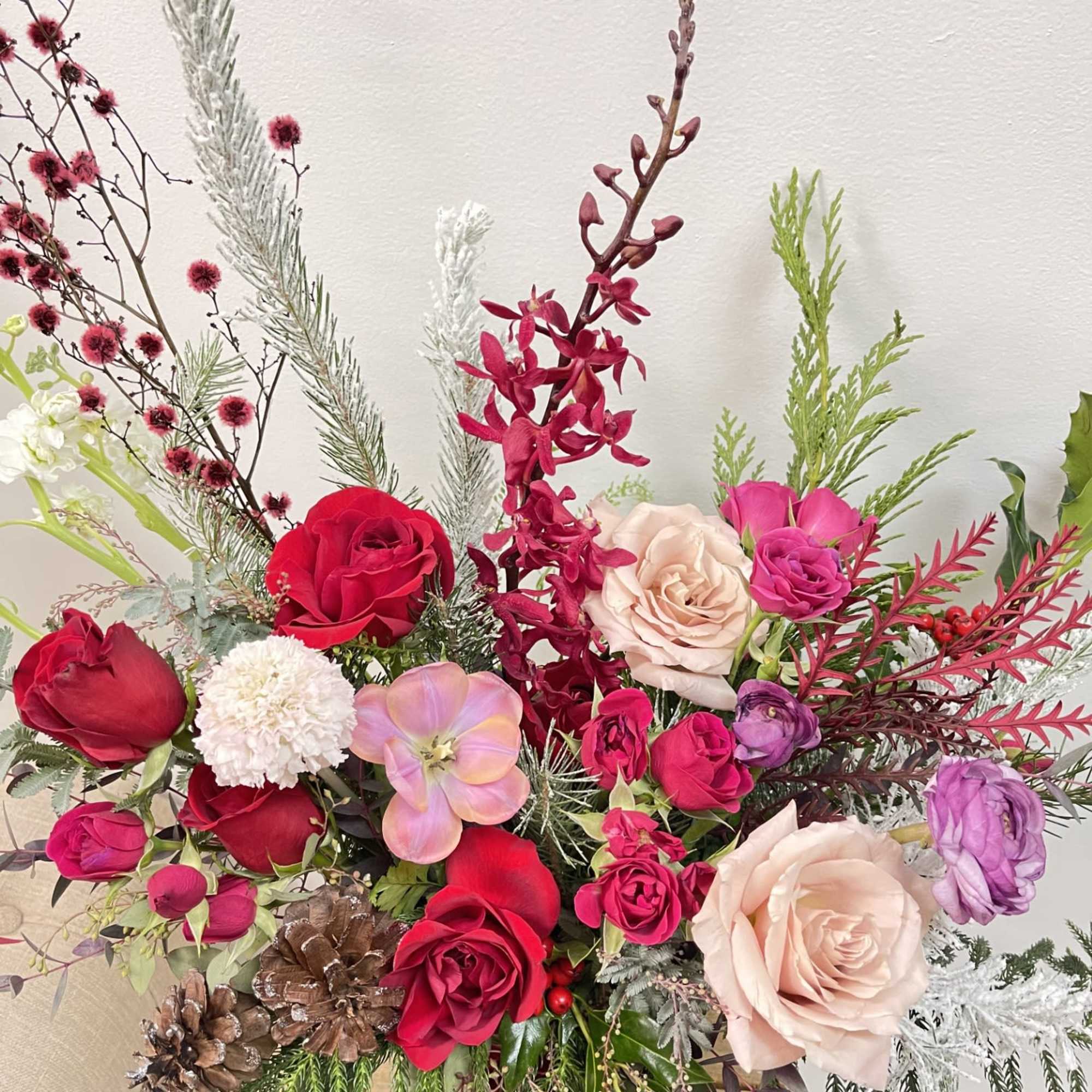 Mixed bouquet of roses and orchids with pinecones and winter greenery