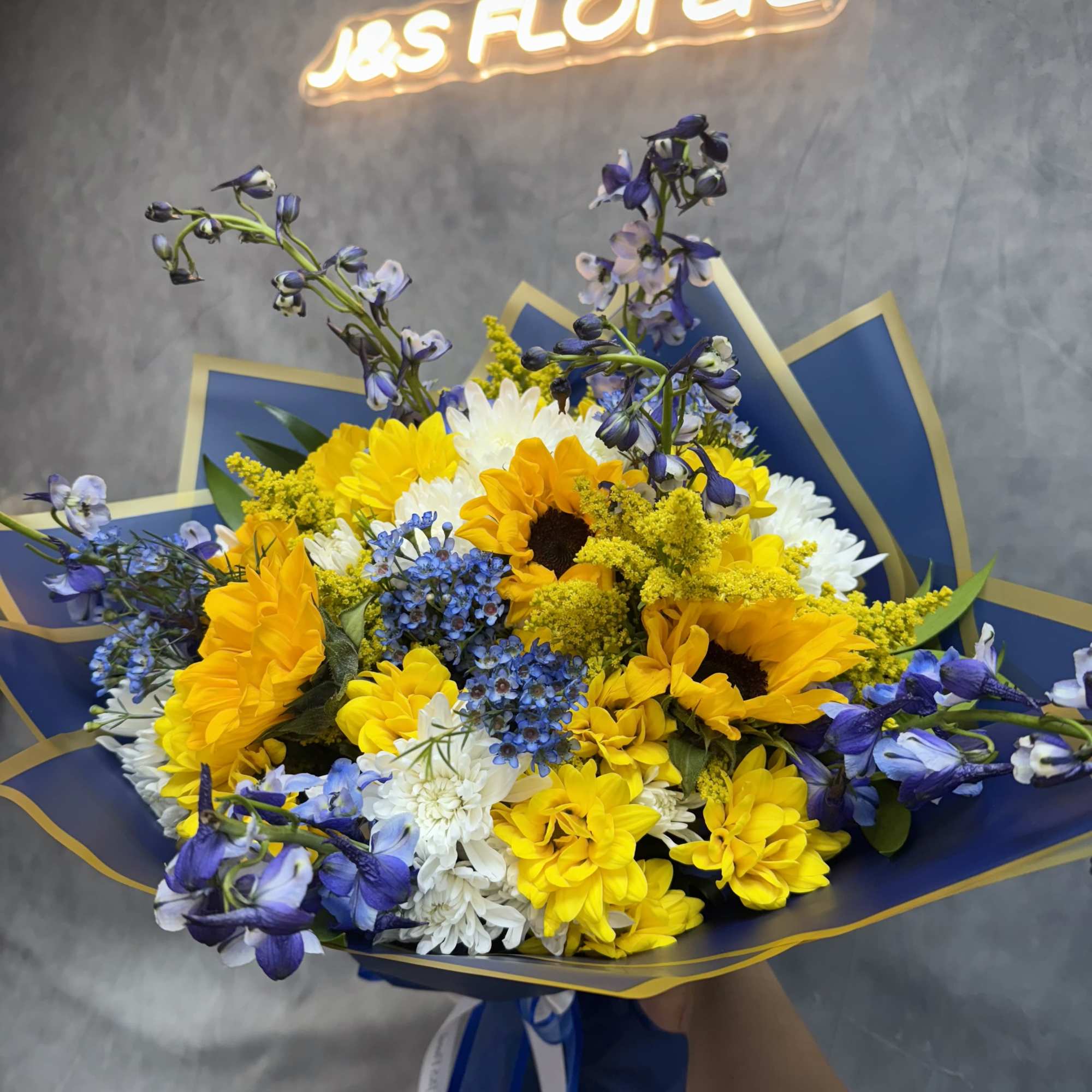 Inspired by Van Gogh, this stunning arrangement features sunflowers, daisies, delphiniums, and