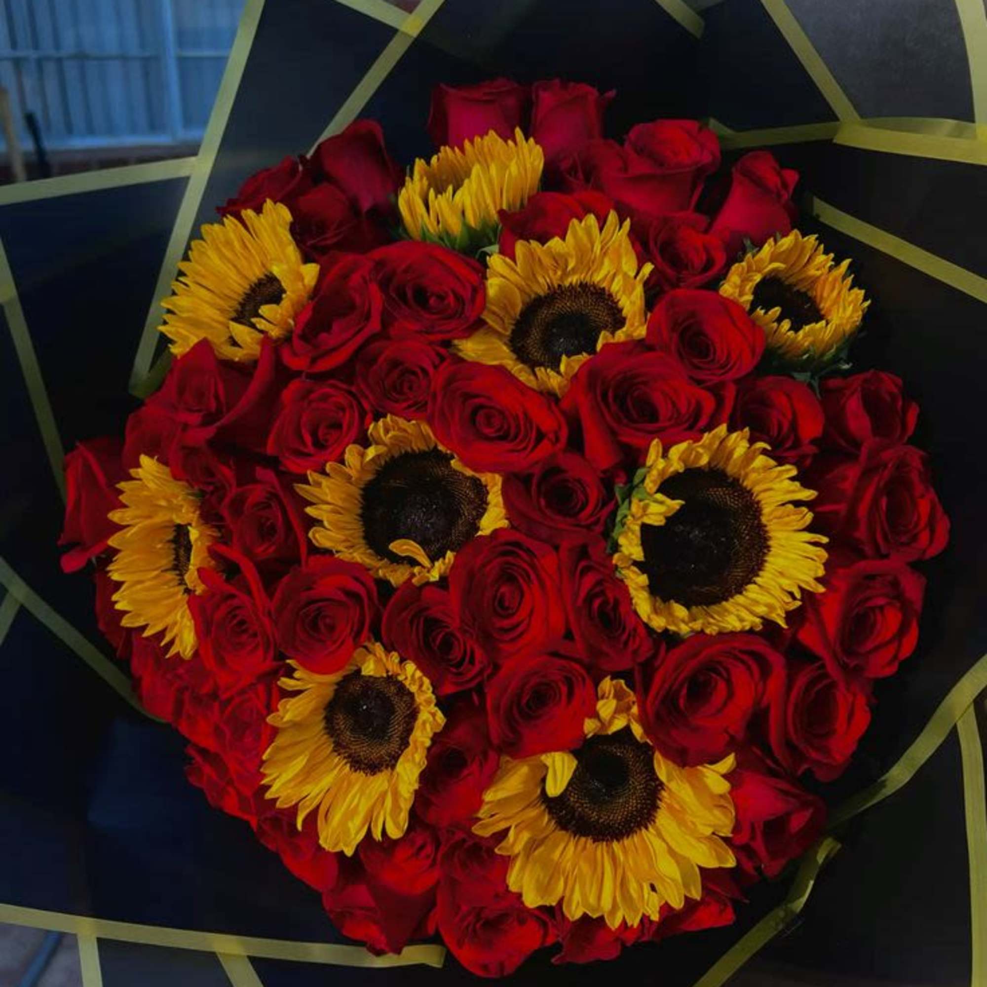 Bouquet of red roses and yellow sunflowers wrapped in black paper