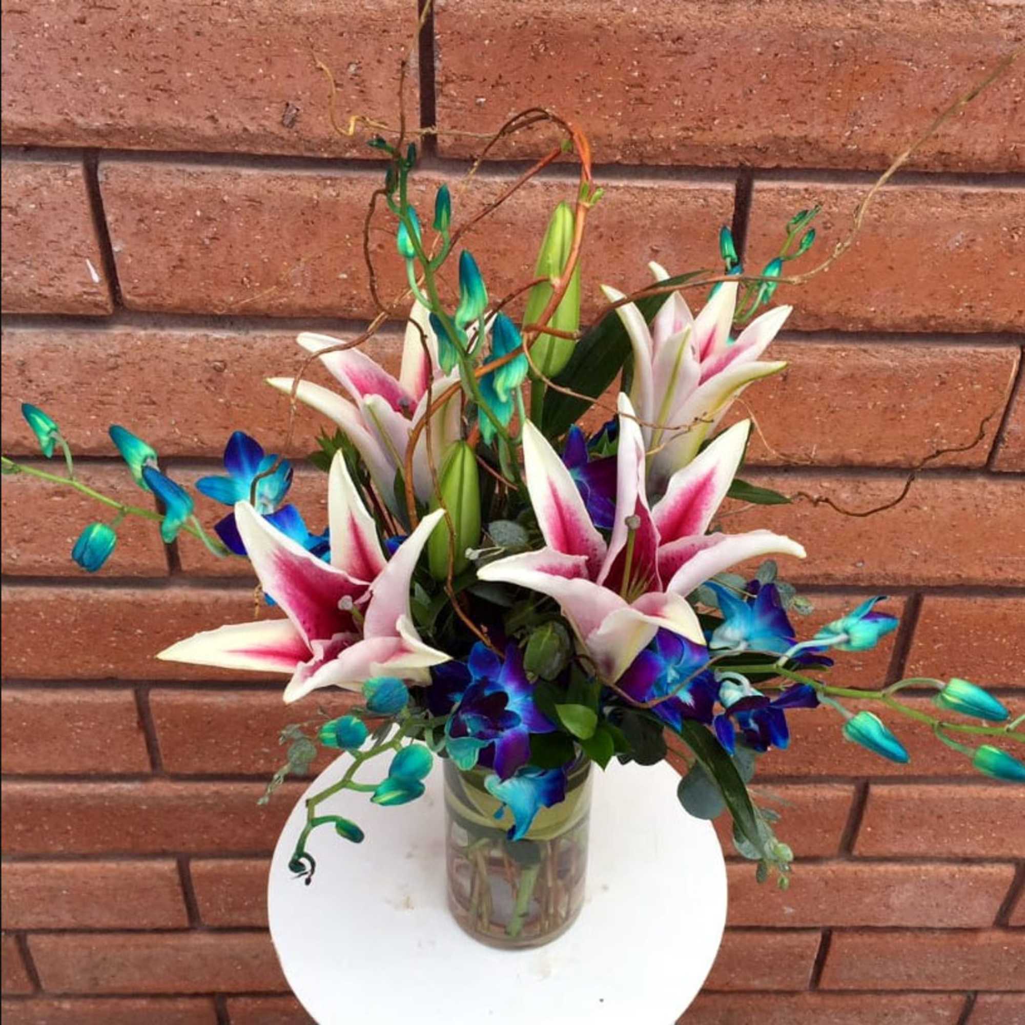 Bouquet of pink-and-white lilies with blue orchids in a glass vase