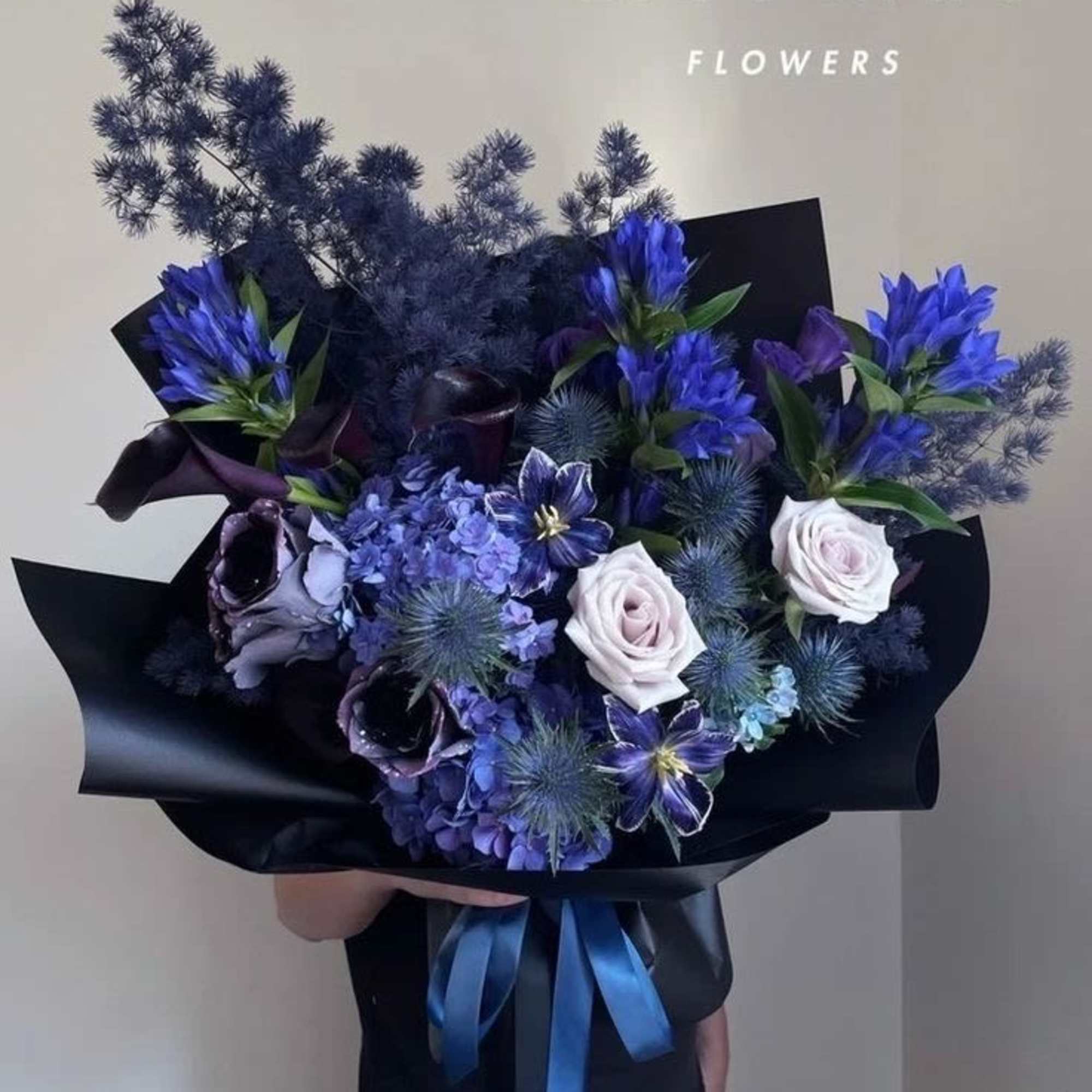 Bouquet of blue and white flowers wrapped in black paper with a blue ribbon