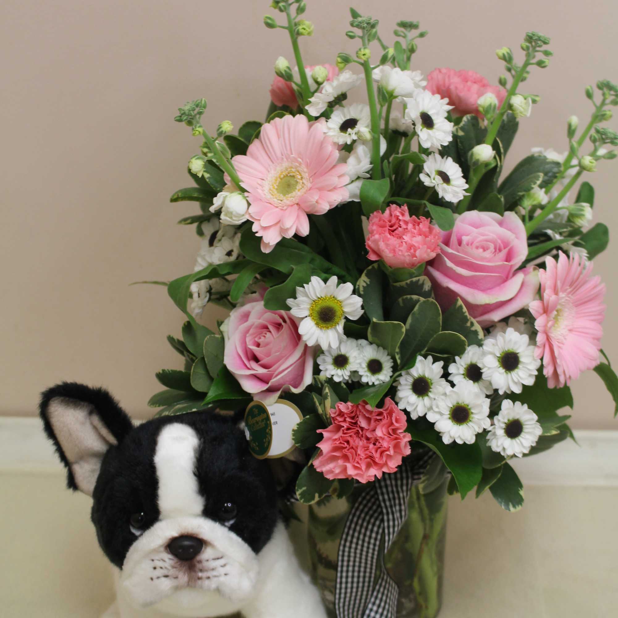 Pink and white flower arrangement with a plush dog in front