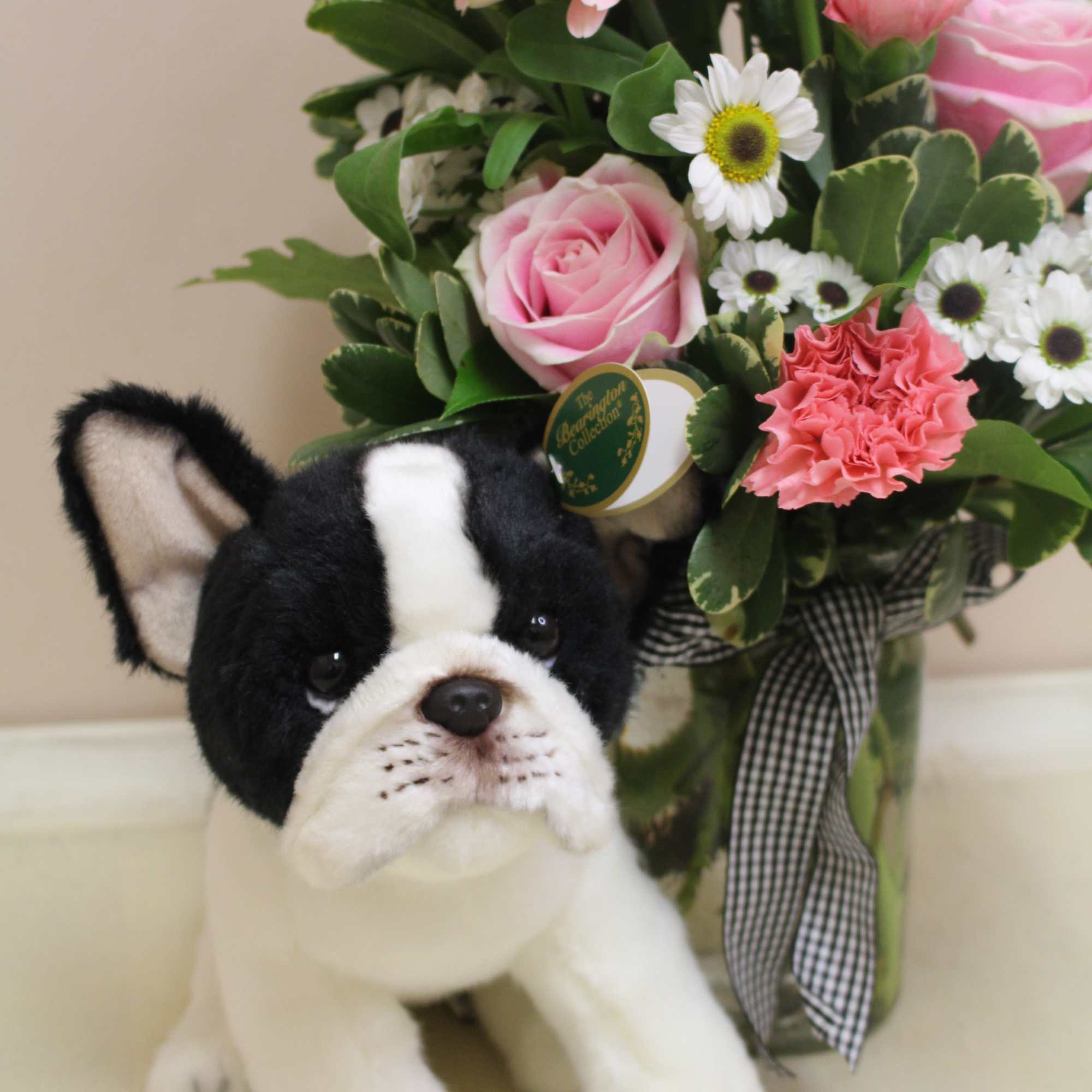 Stuffed dog beside a pink and white flower arrangement