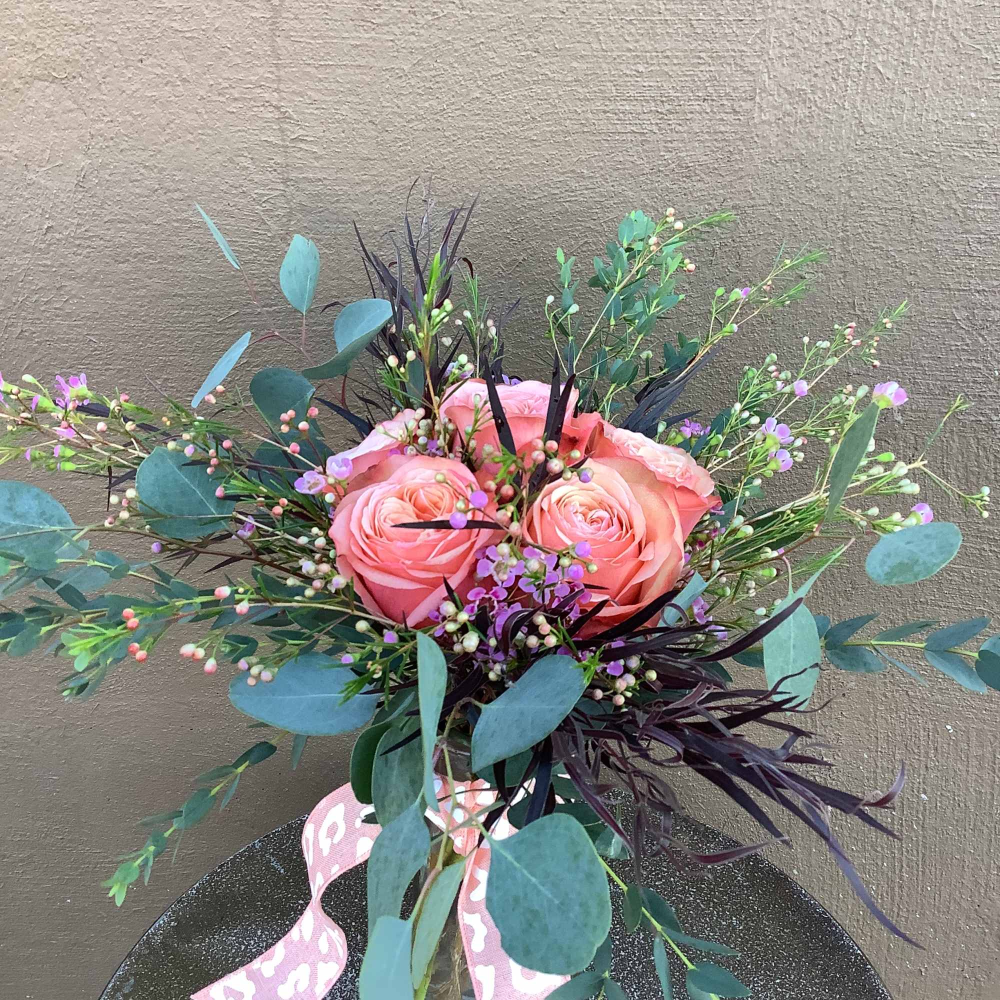 Pink roses in a glass vase with eucalyptus and small purple filler flowers