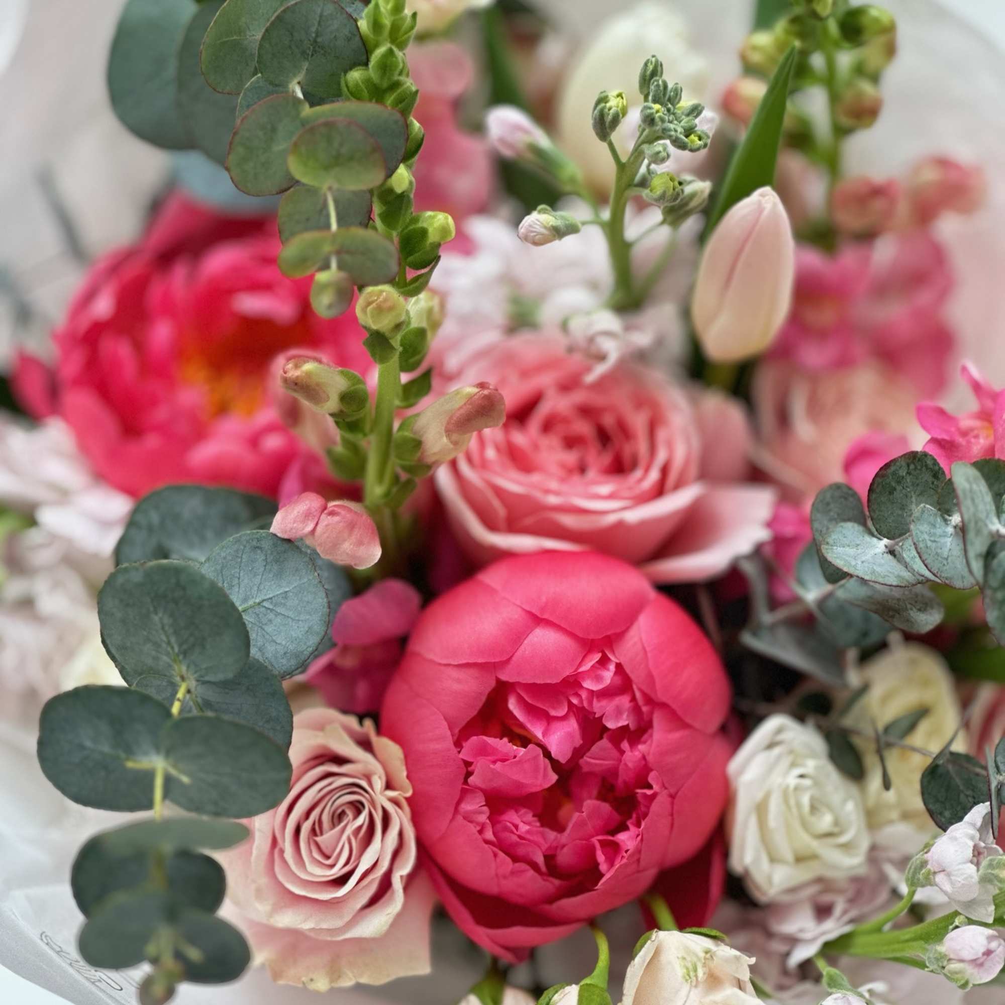 Hand-tied bouquet of bright pink peonies, pale roses, snapdragons, a tulip and eucalyptus.