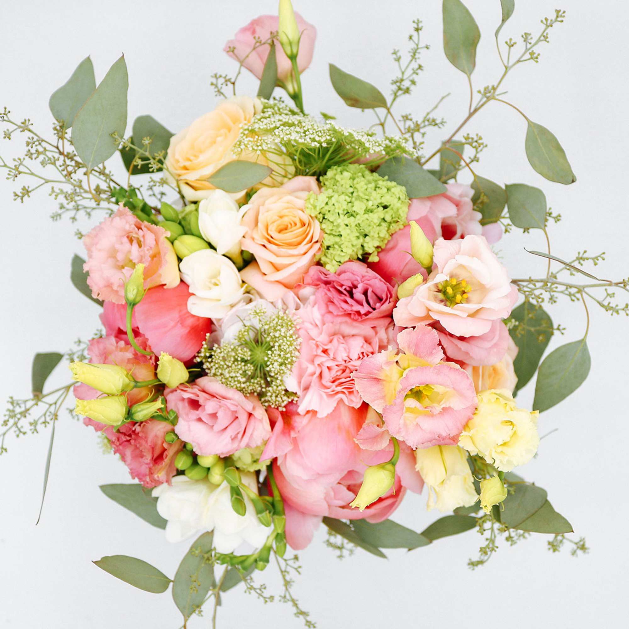 Top view of a pastel bouquet with pink peonies, peach roses, and cream blossoms.
