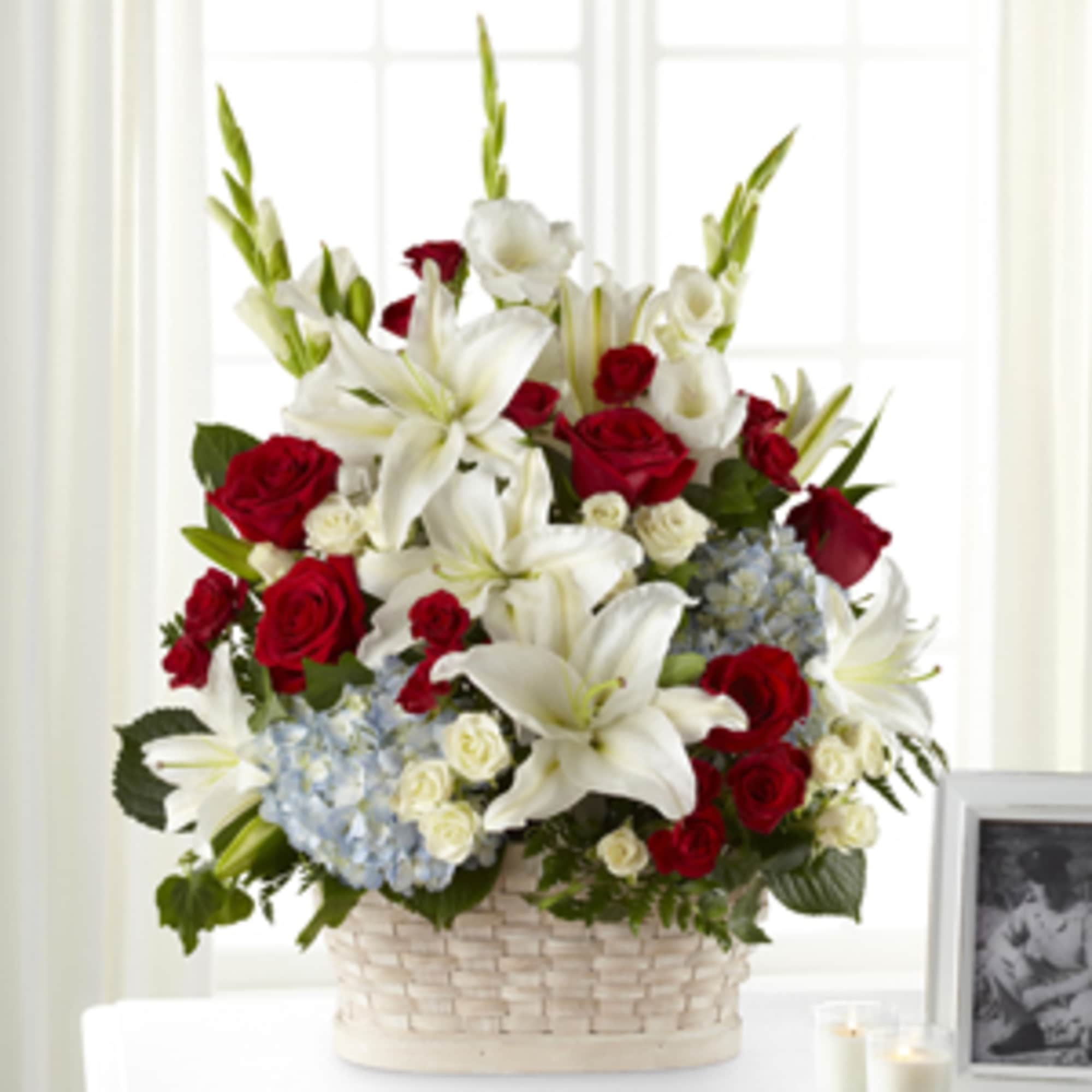 Basket arrangement of red roses, white lilies, and blue hydrangeas