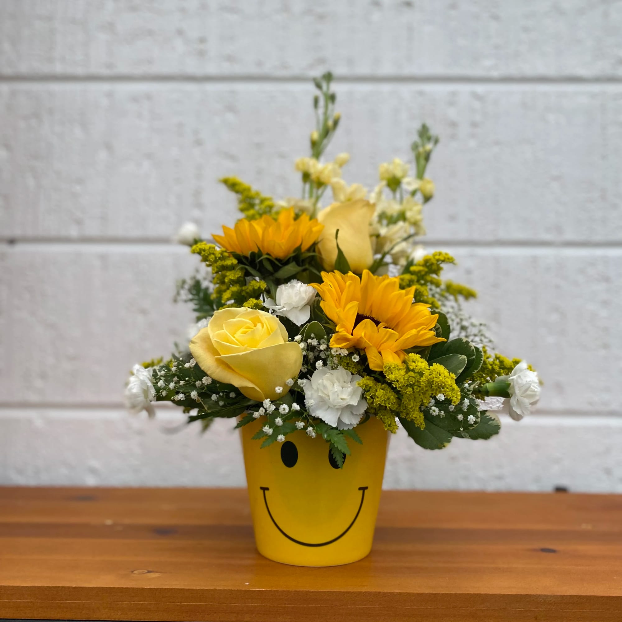 Yellow floral arrangement in a smiley-face pot with roses and sunflowers