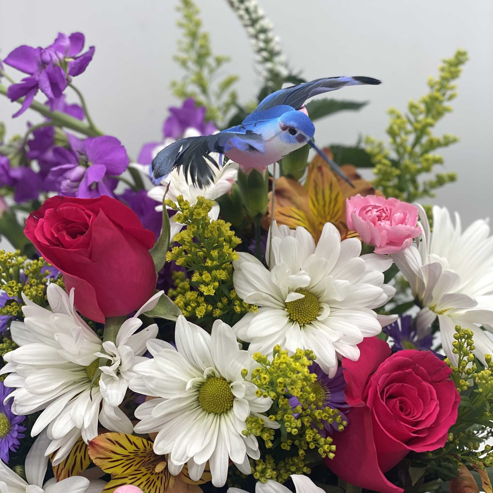 Mixed bouquet with roses, daisies, and a small blue bird decoration