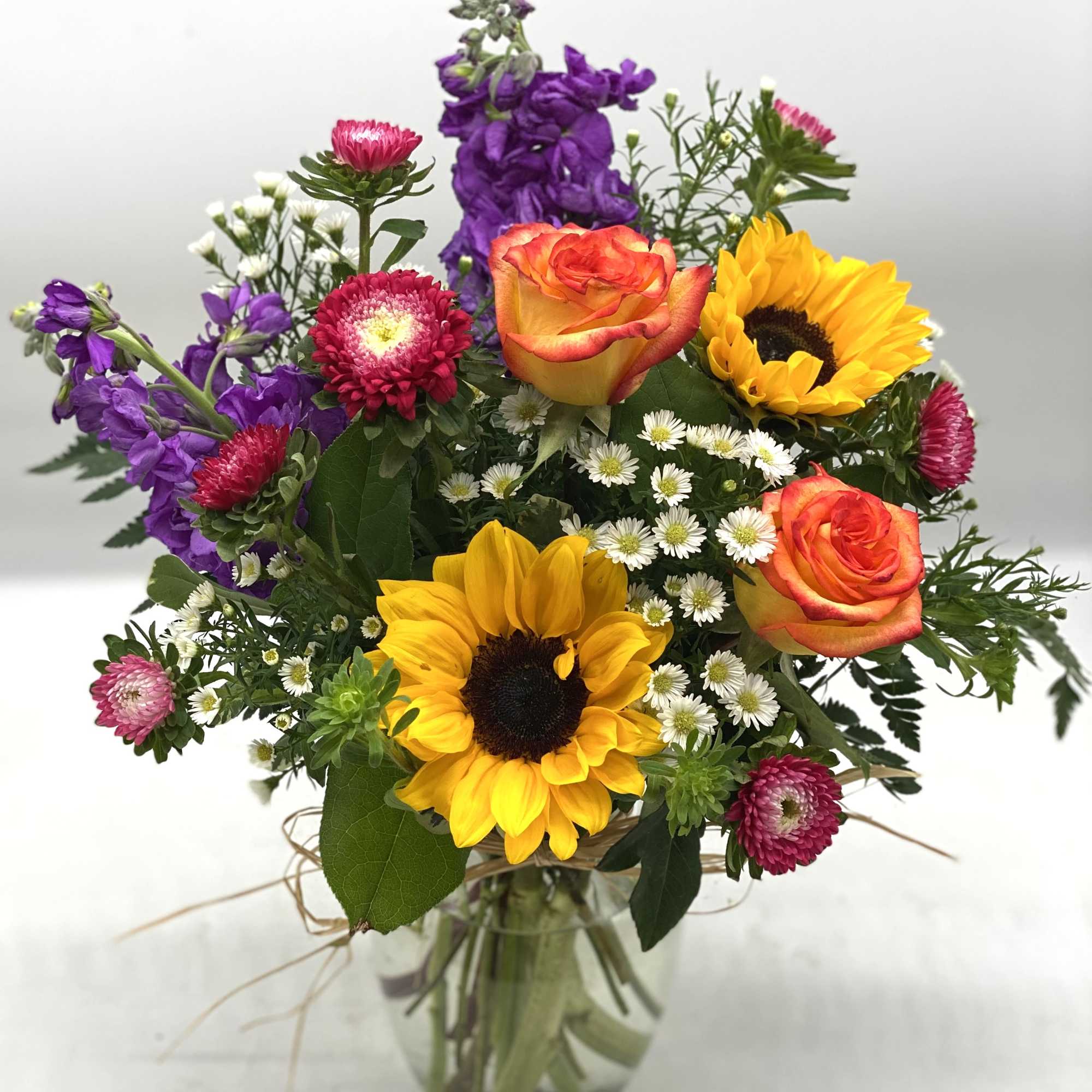 Mixed bouquet with sunflowers, roses, and purple blooms in a glass vase