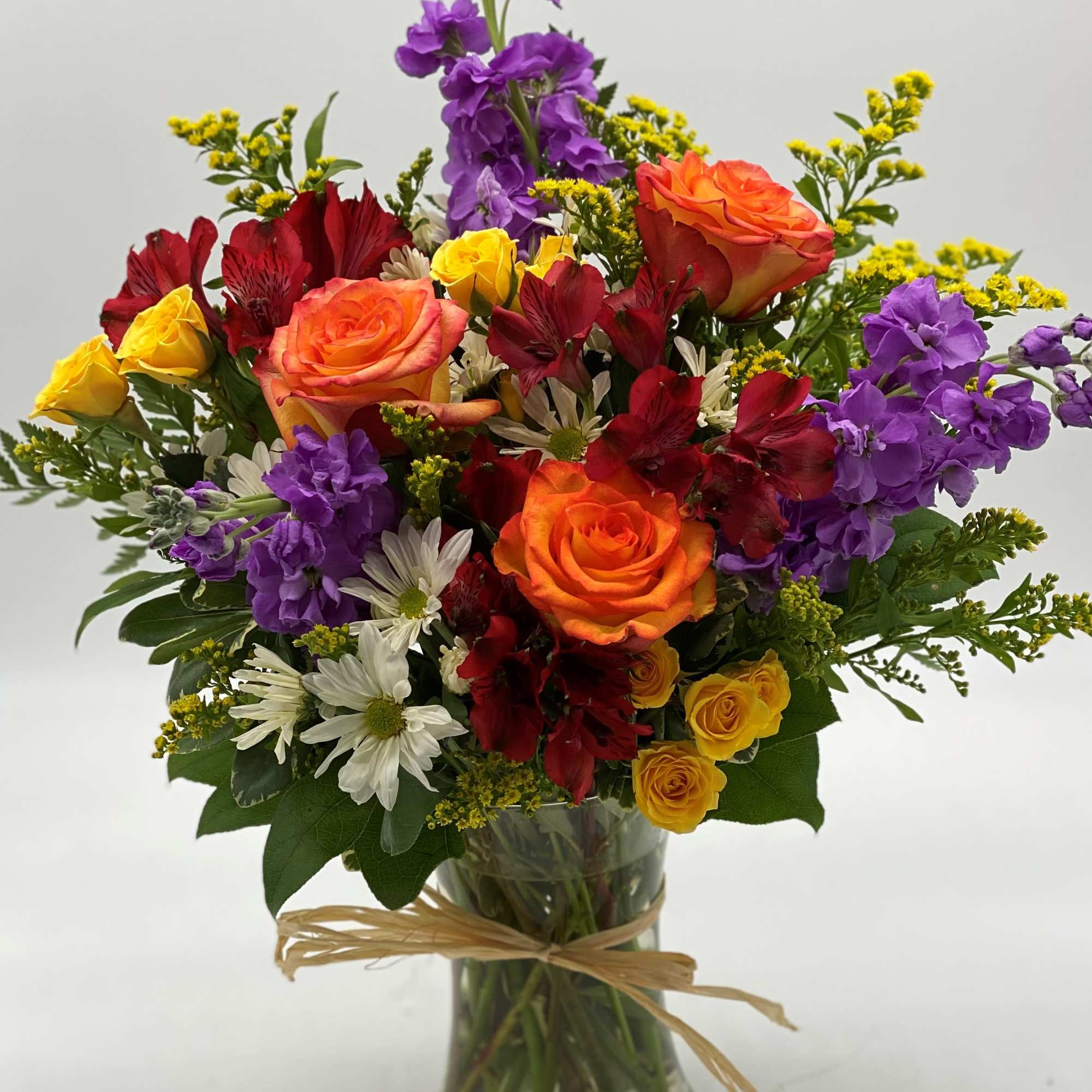 Mixed bouquet of roses, purple stock, and daisies in a glass vase