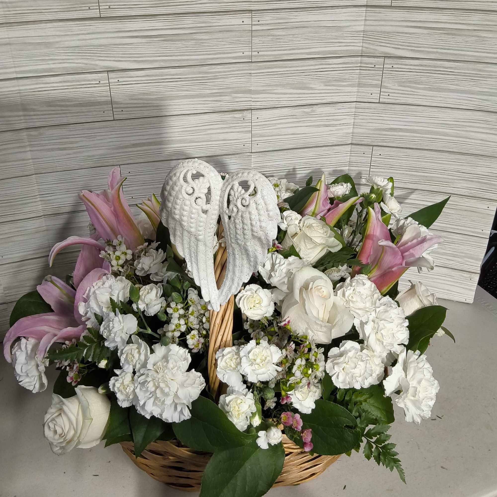 Basket arrangement of white roses, carnations, and pink lilies with angel wings