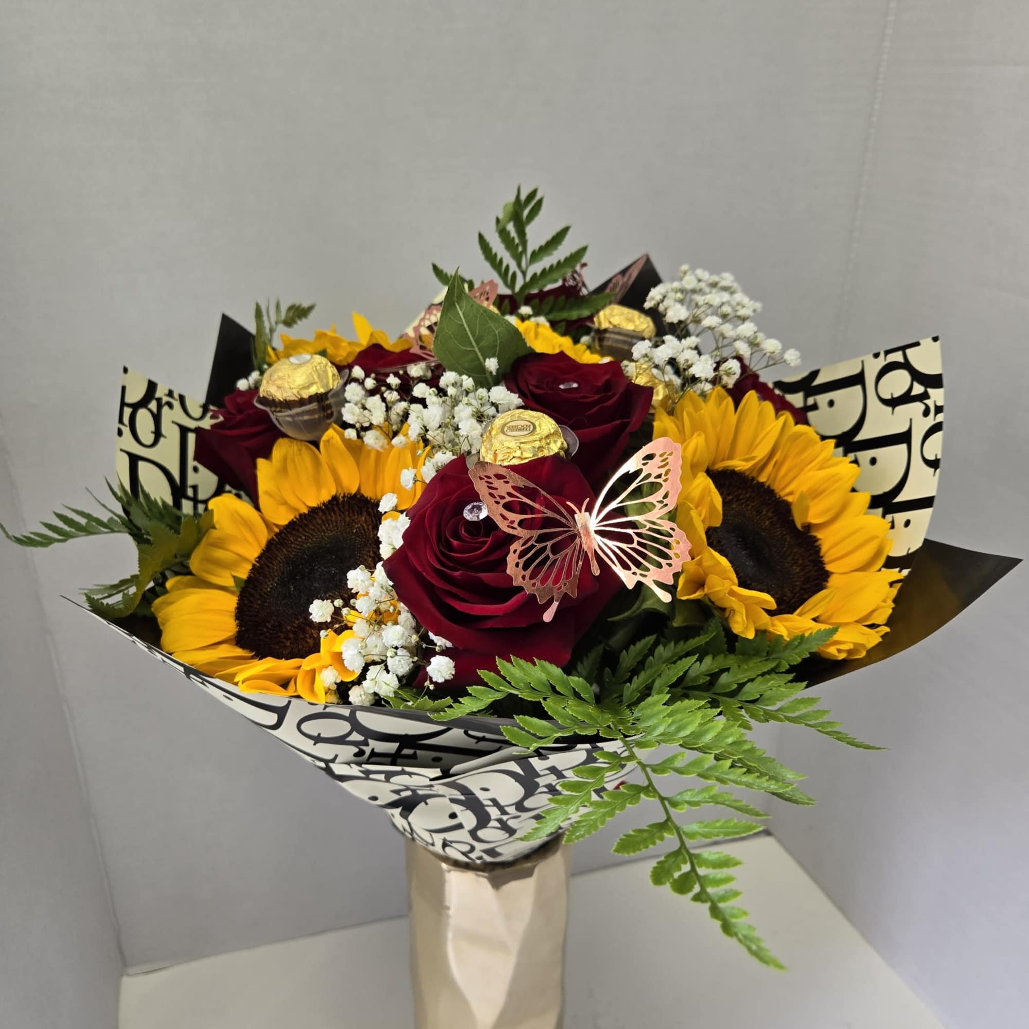 Bouquet of red roses and sunflowers with chocolates in a wrapped vase