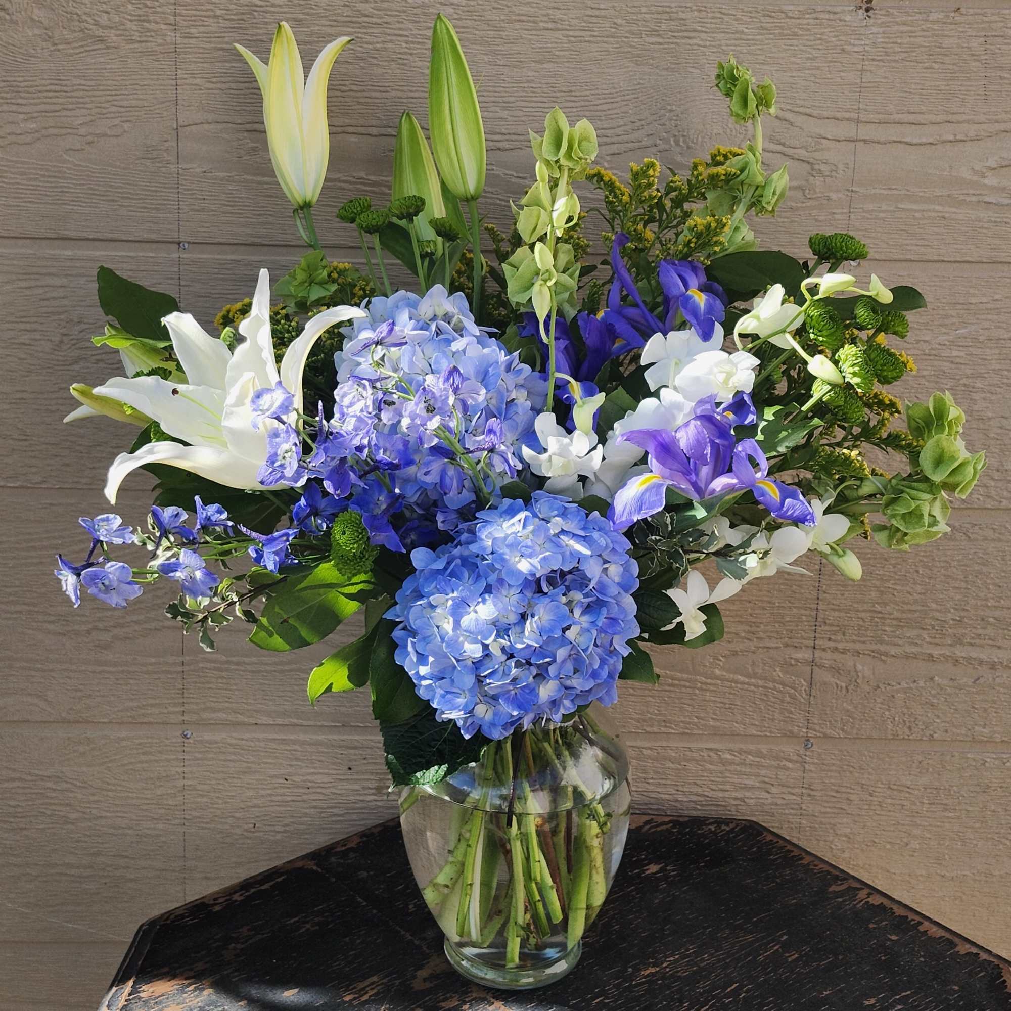 This arrangement contains delphinium, bells of ireland, asiatic lilies, hydrangea, blue iris