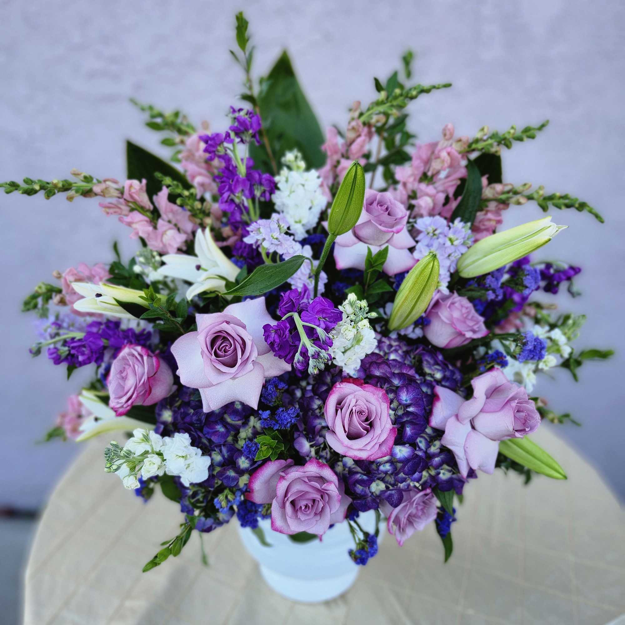 A purple and white sympathy basket featuring snapdragons, roses, lilies, and stock.