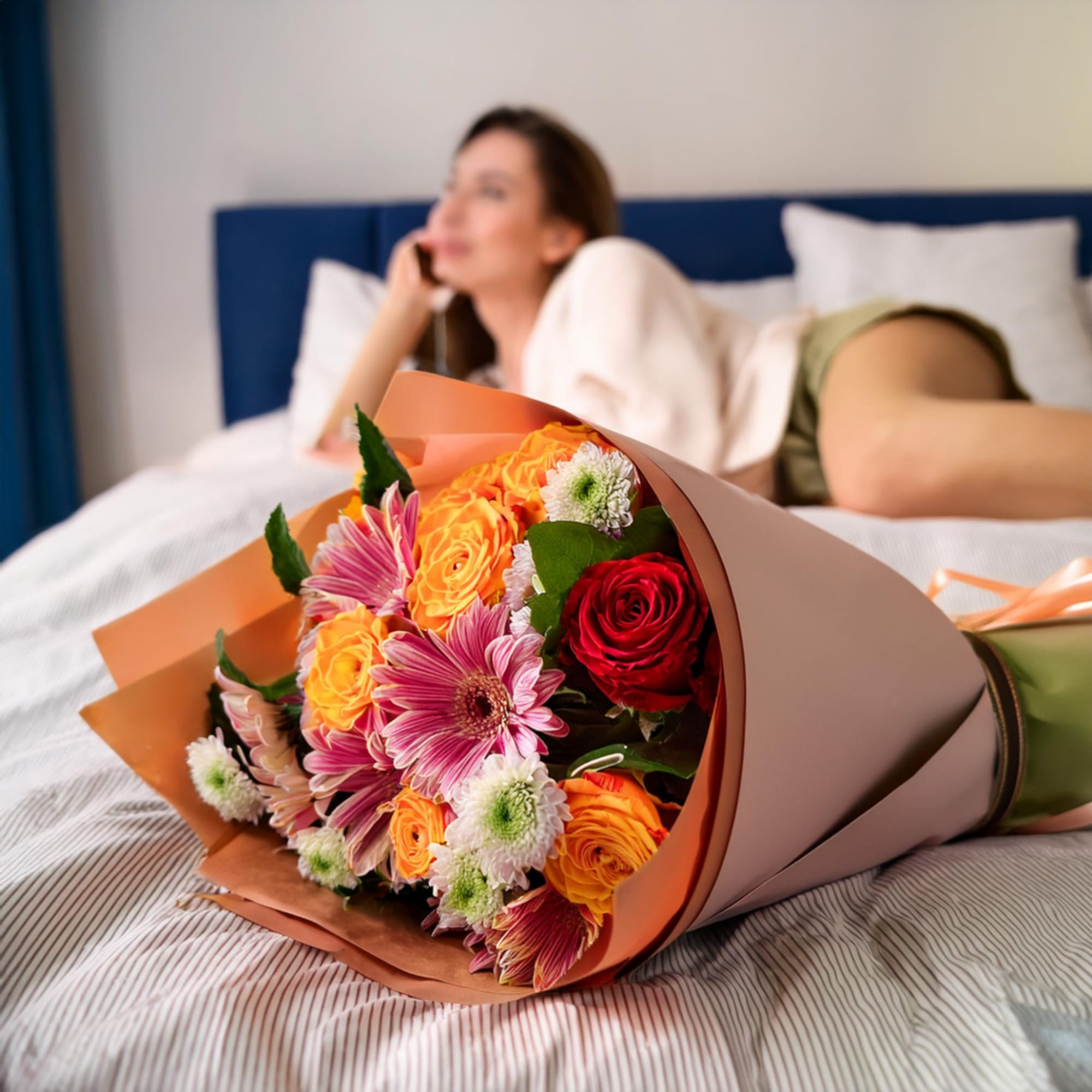 Bouquet of orange, pink, and red flowers wrapped in paper on a bed