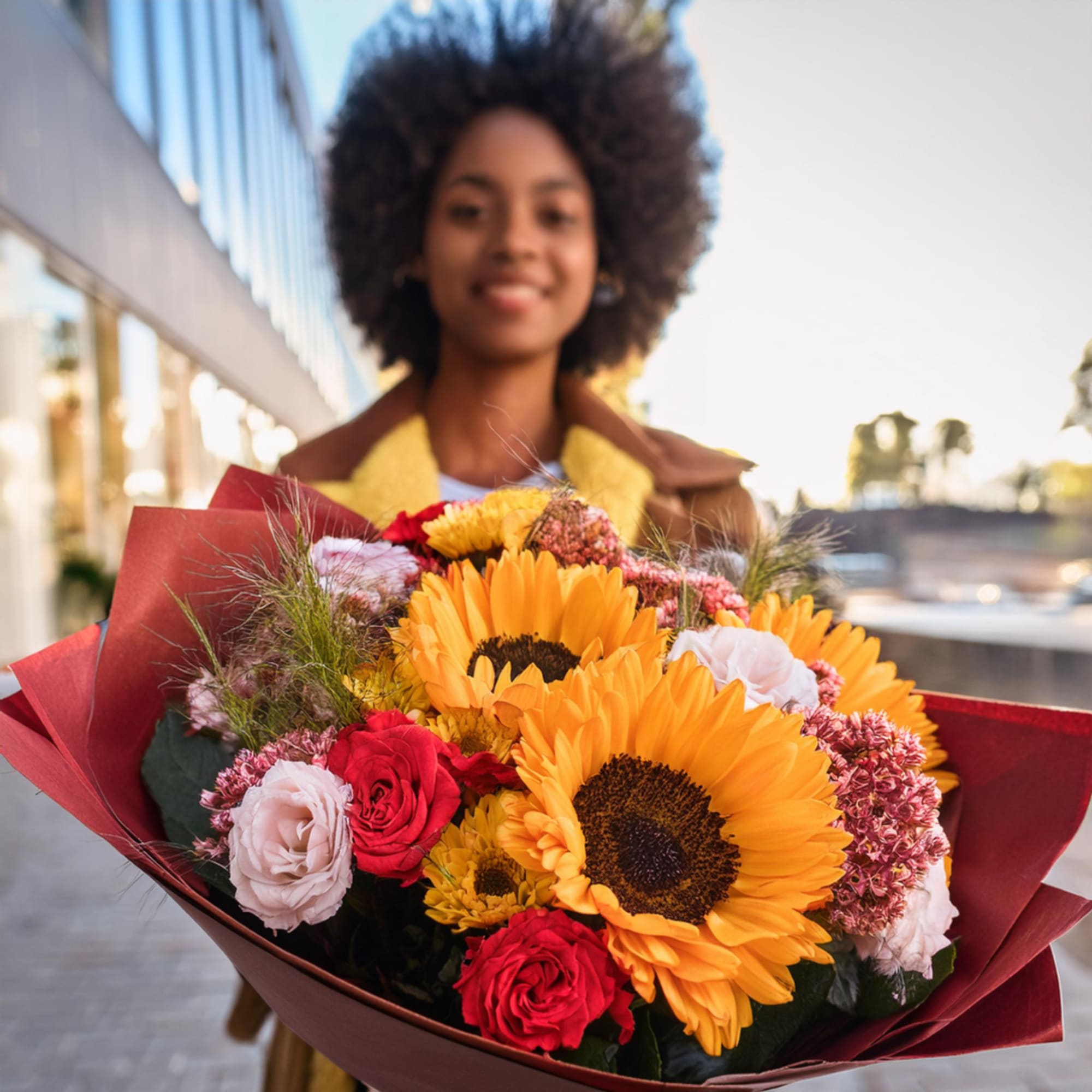 Bouquet of sunflowers, red roses, and pale pink blooms wrapped in burgundy paper