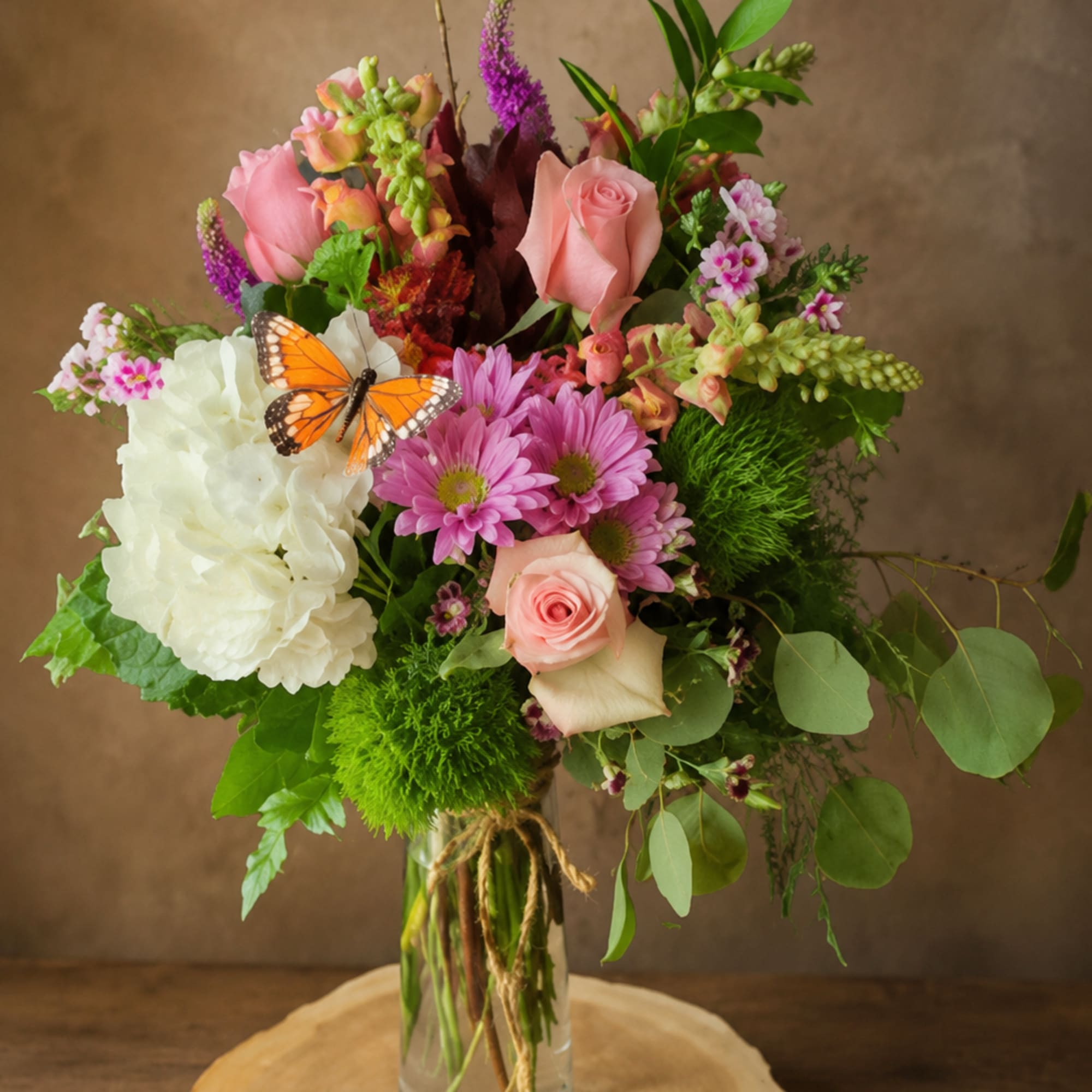 Mixed bouquet of pink and white flowers in a glass vase with a butterfly accent
