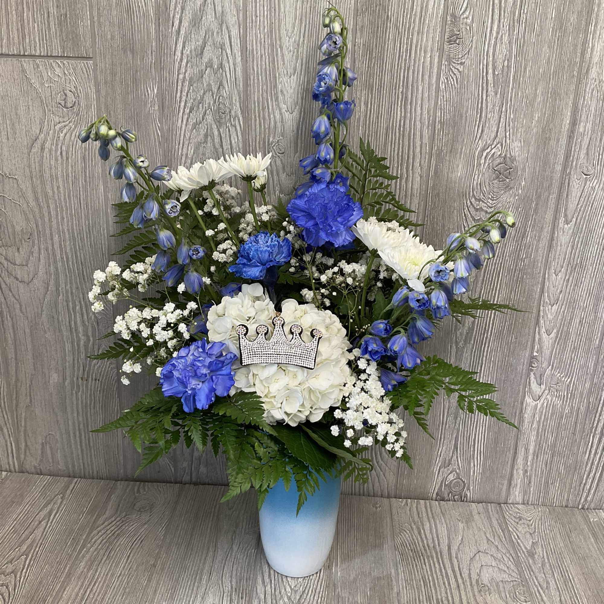 Blue and white floral arrangement in a vase with a crown ornament